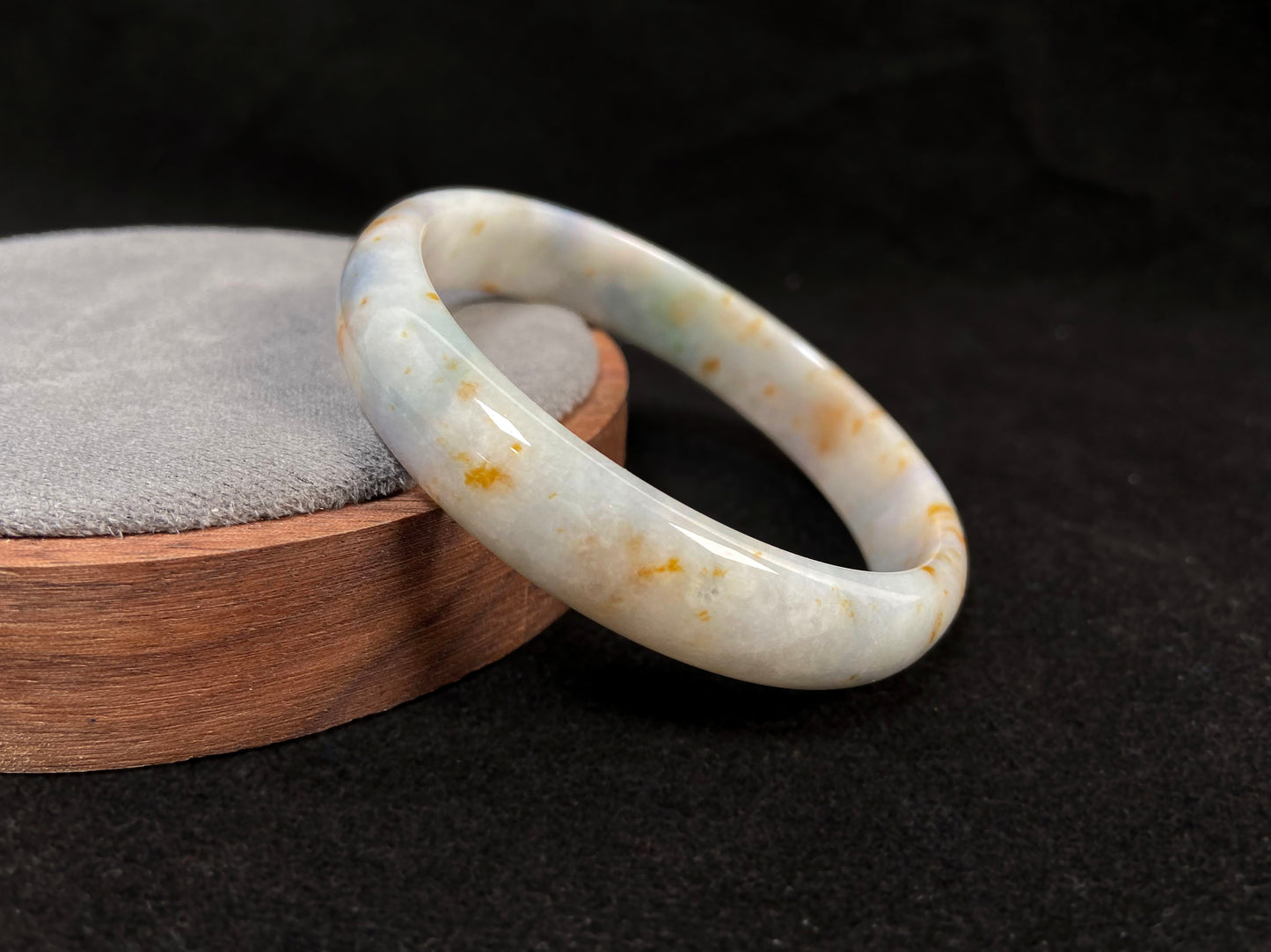 A white jade bracelet adorned with golden speckles and deep green flashes.
