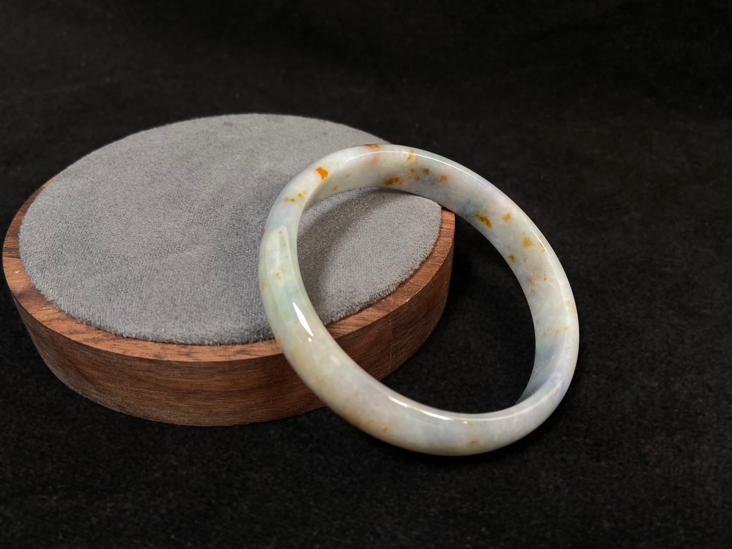 A white jade bracelet adorned with golden speckles and deep green flashes.