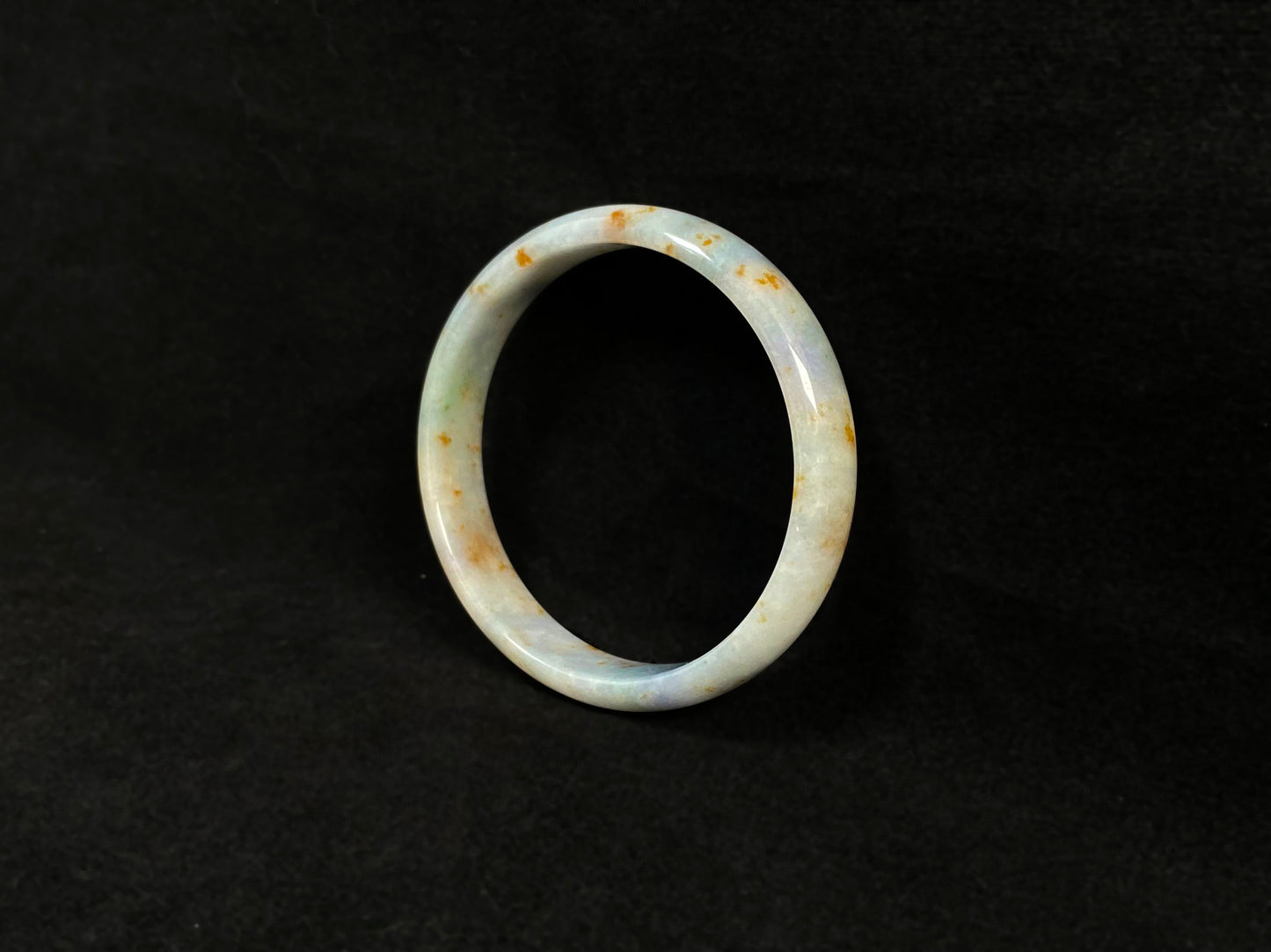 A white jade bracelet adorned with golden speckles and deep green flashes.