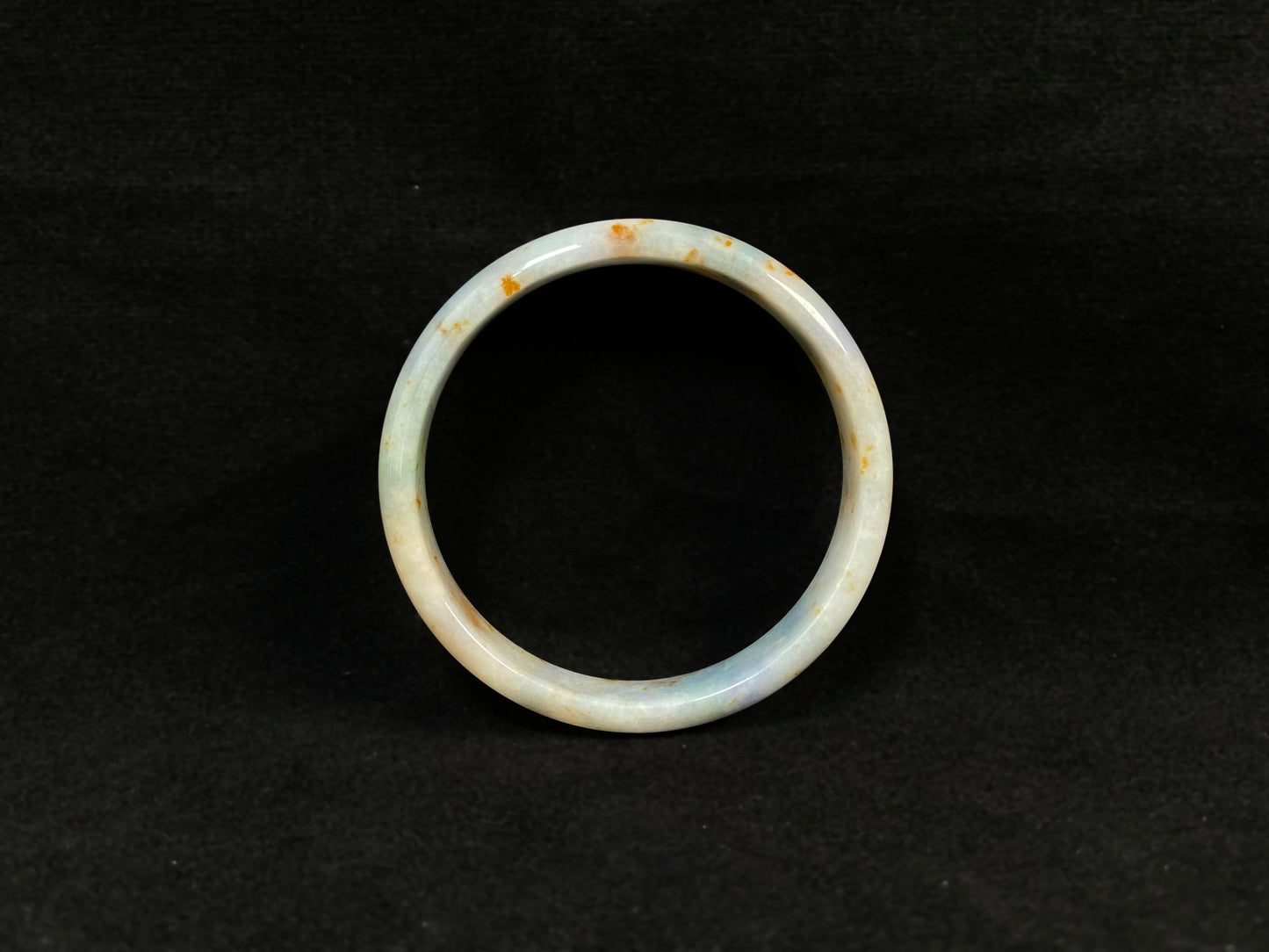 A white jade bracelet adorned with golden speckles and deep green flashes.