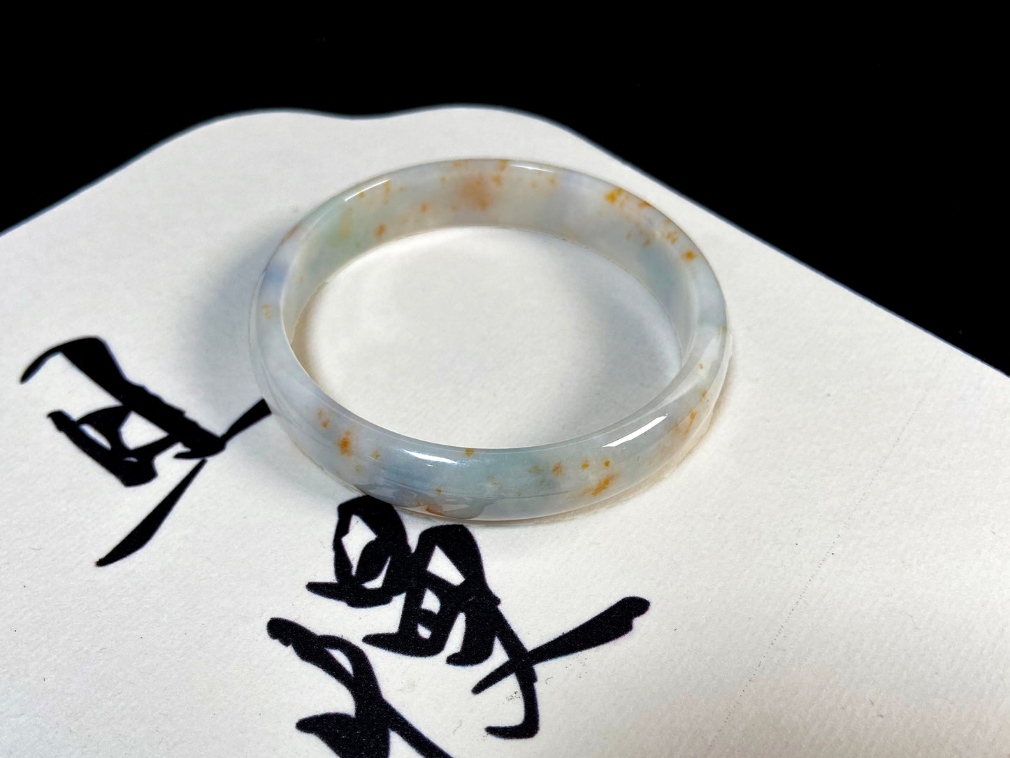 A white jade bracelet adorned with golden speckles and deep green flashes.