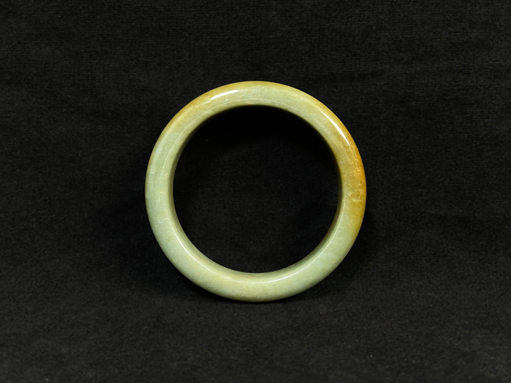 A white and green jade bracelet bathed in golden shimmer.