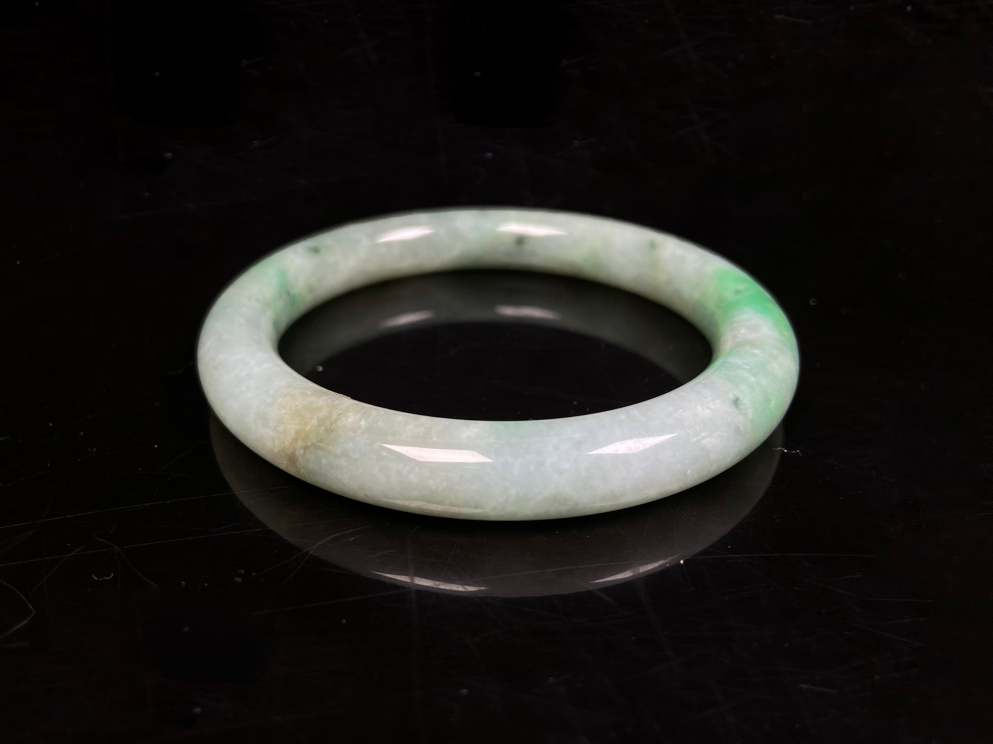 A pale white cyan base with lively green accents  jadeite bangle.