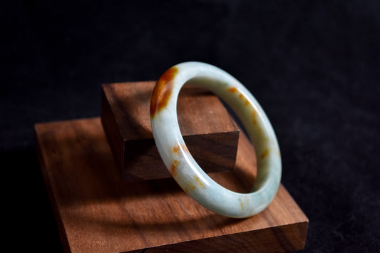 White jade bracelet with brown spots on a wooden stand against a dark background