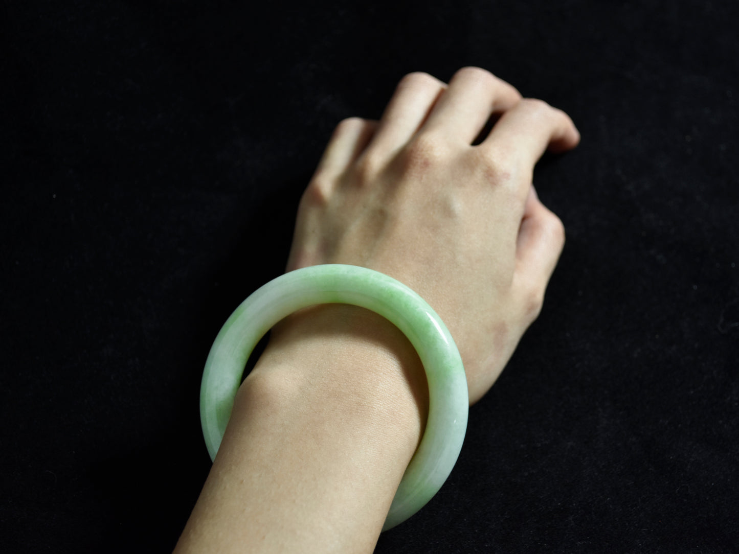 Hand wearing a green jade bracelet against a black background
