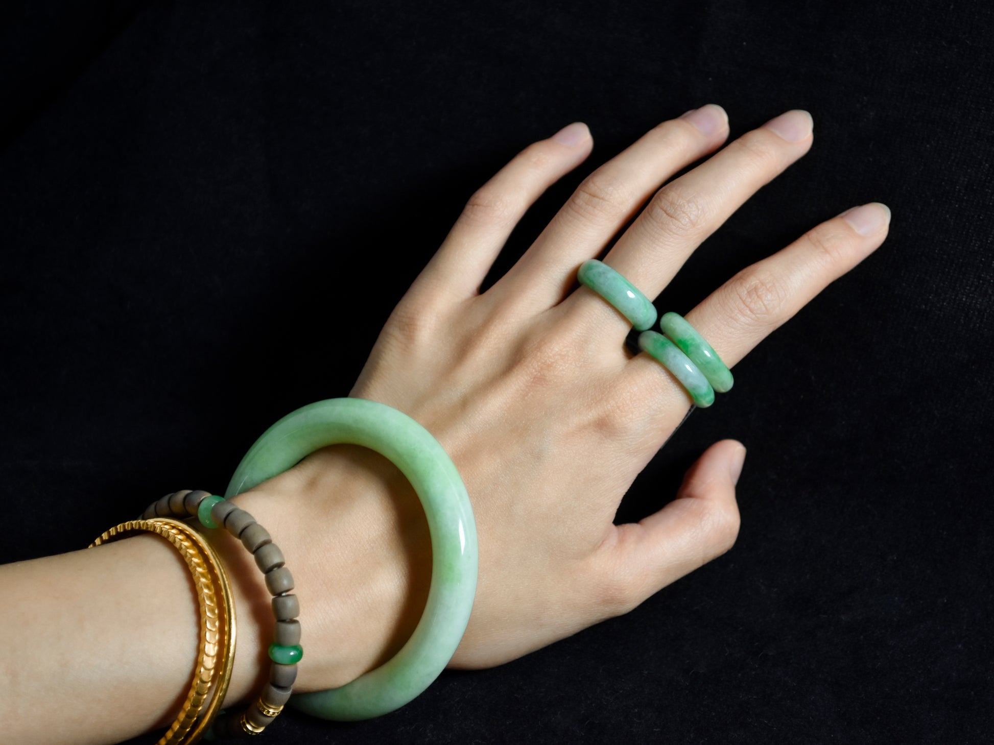 Hand wearing multiple jade bracelets on a black background