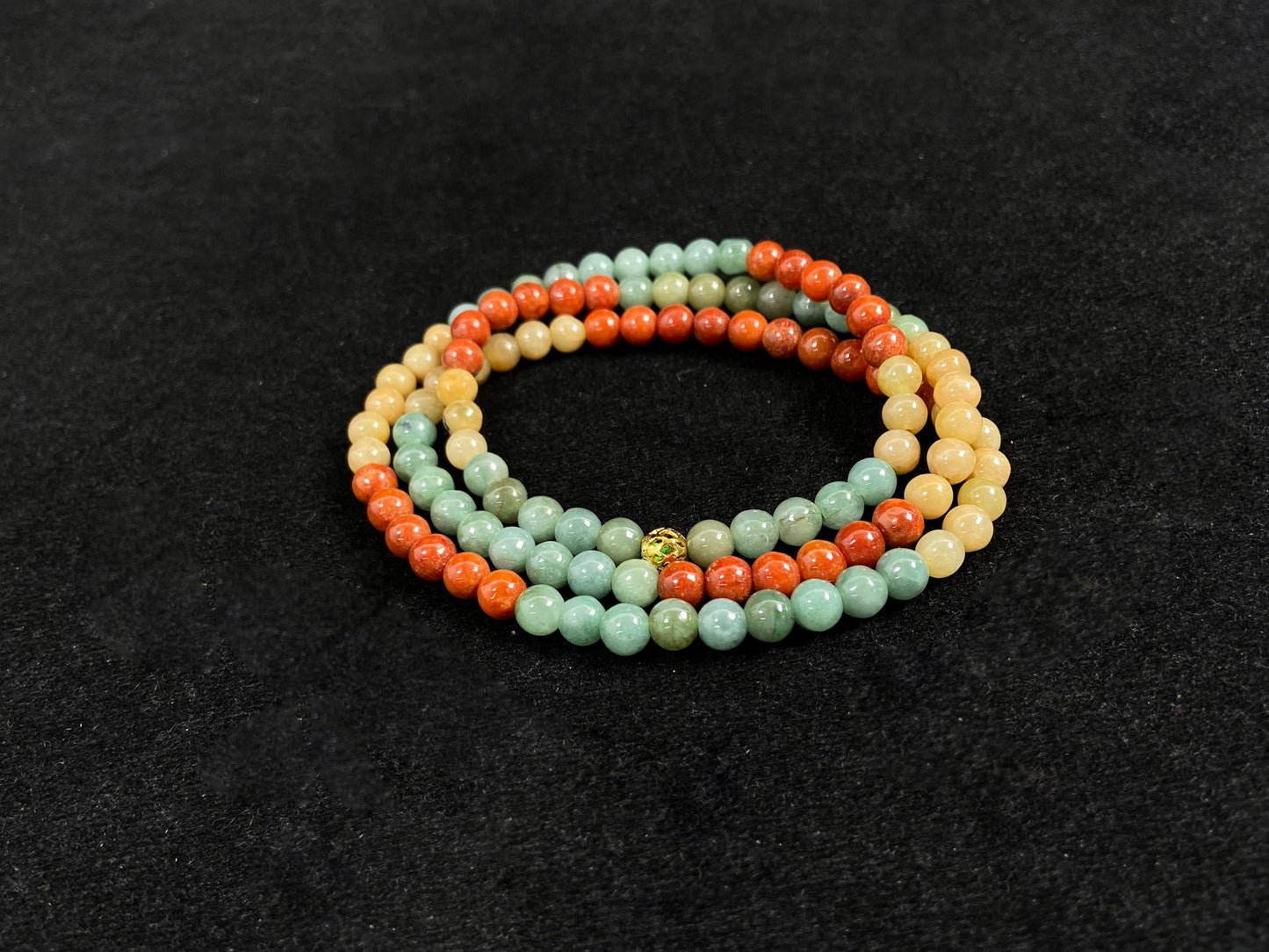 This jade necklace features a repeating pattern of six yellow, six light green, and six orange-red beads, accented with a central golden focal bead.