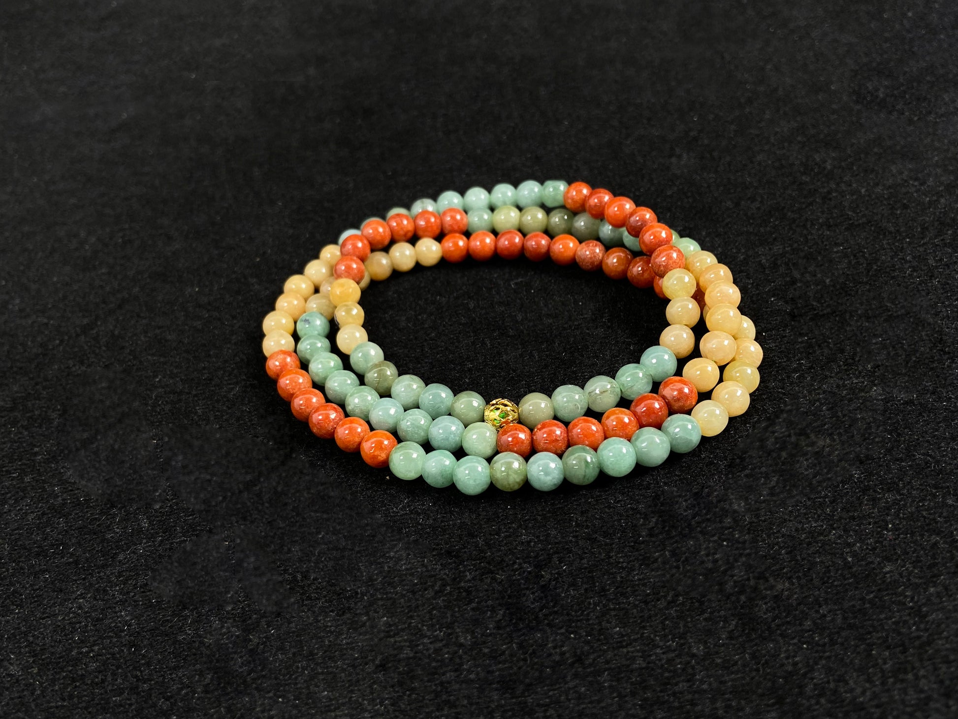 This jade necklace features a repeating pattern of six yellow, six light green, and six orange-red beads, accented with a central golden focal bead.