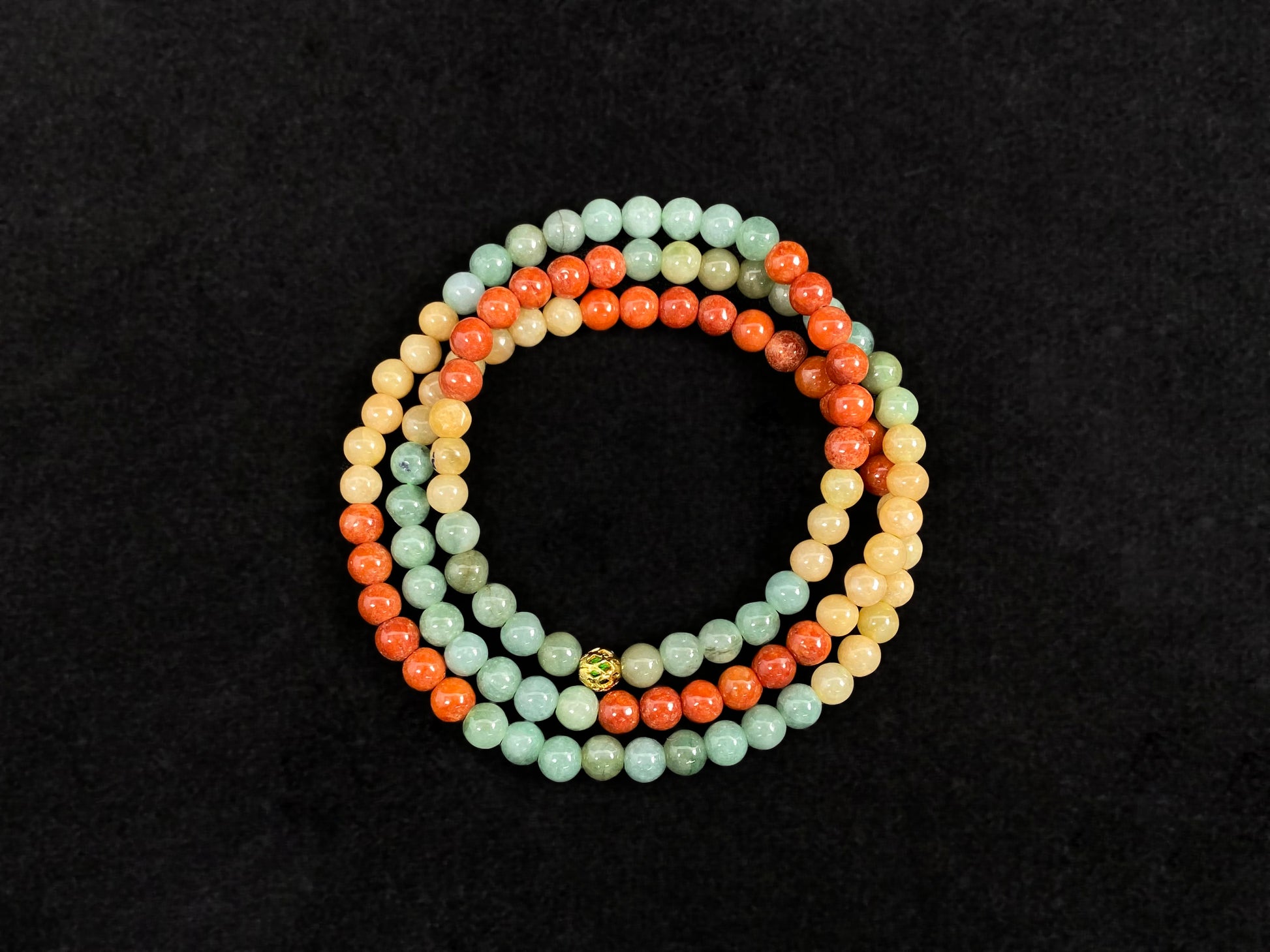 This jade necklace features a repeating pattern of six yellow, six light green, and six orange-red beads, accented with a central golden focal bead.