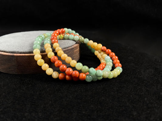 This jade necklace features a repeating pattern of six yellow, six light green, and six orange-red beads, accented with a central golden focal bead.