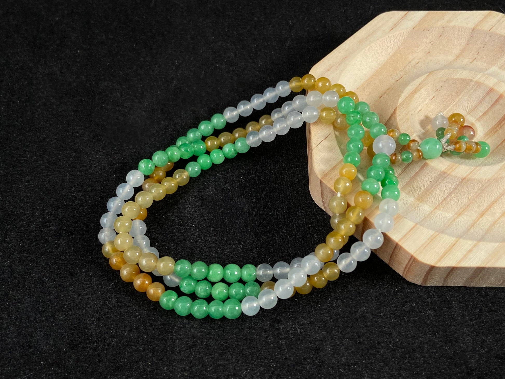 This jade bead strand alternates clusters of apple green, yellow, transparent white, and brown beads in a rhythmic color pattern.