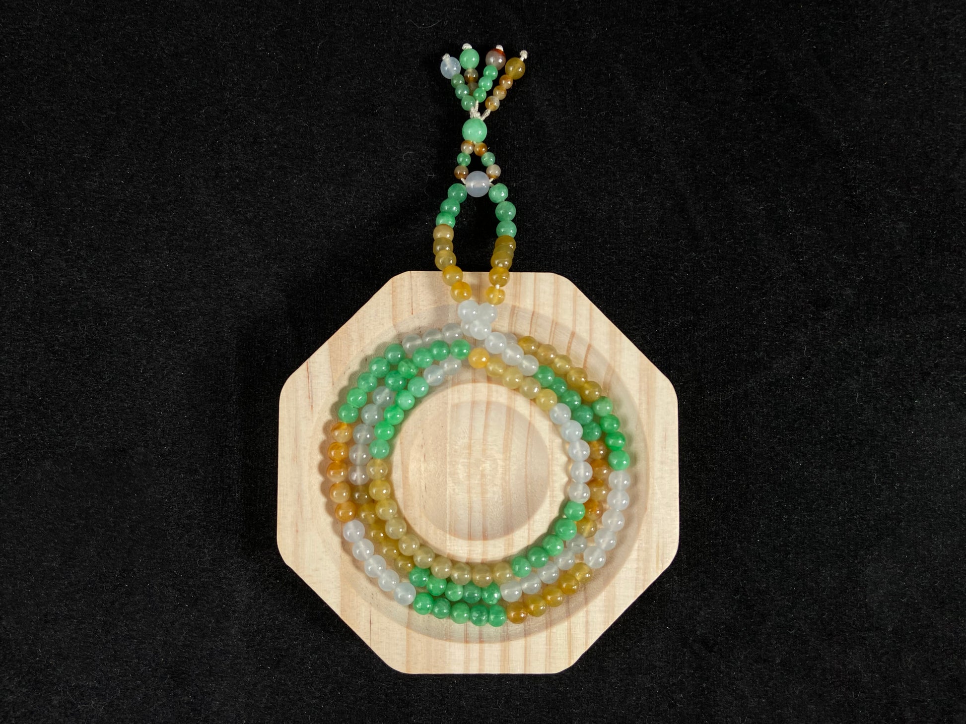 This jade bead strand alternates clusters of apple green, yellow, transparent white, and brown beads in a rhythmic color pattern.