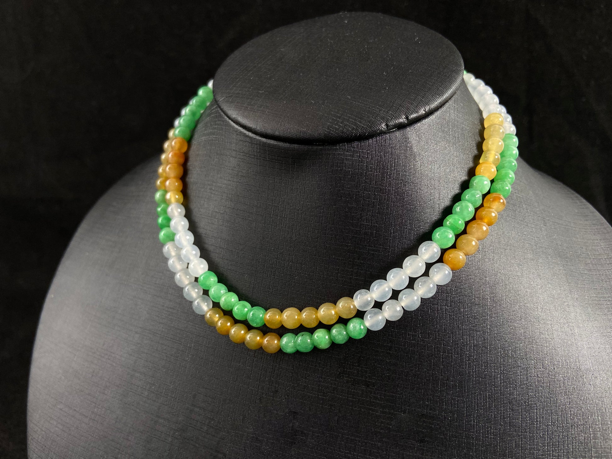 This jade bead strand alternates clusters of apple green, yellow, transparent white, and brown beads in a rhythmic color pattern.