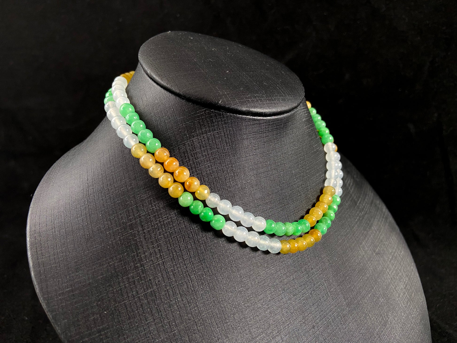 This jade bead strand alternates clusters of apple green, yellow, transparent white, and brown beads in a rhythmic color pattern.