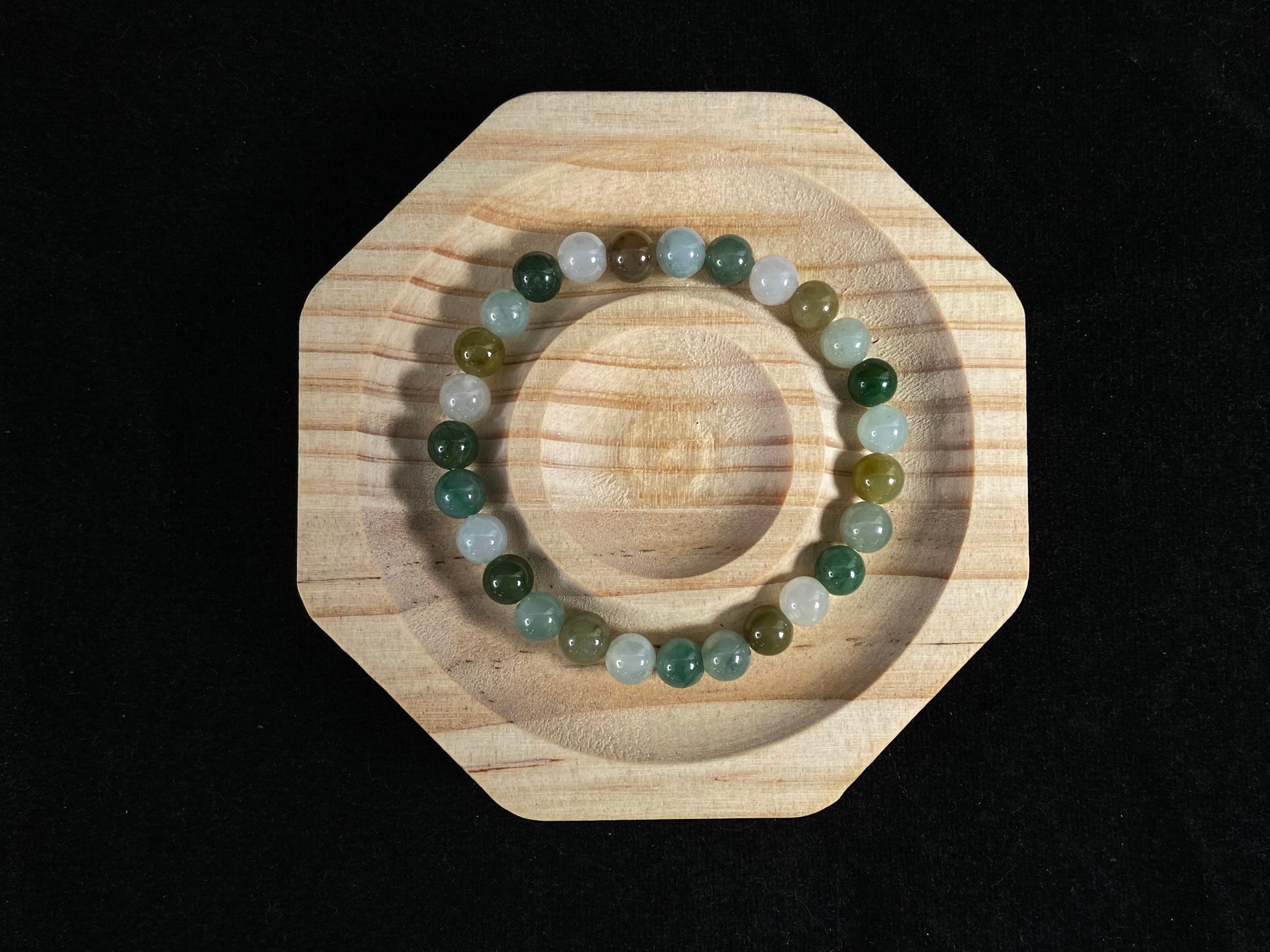 A strand of uniform jade beads in icy white, light green, deep green, pale yellow, and brown.