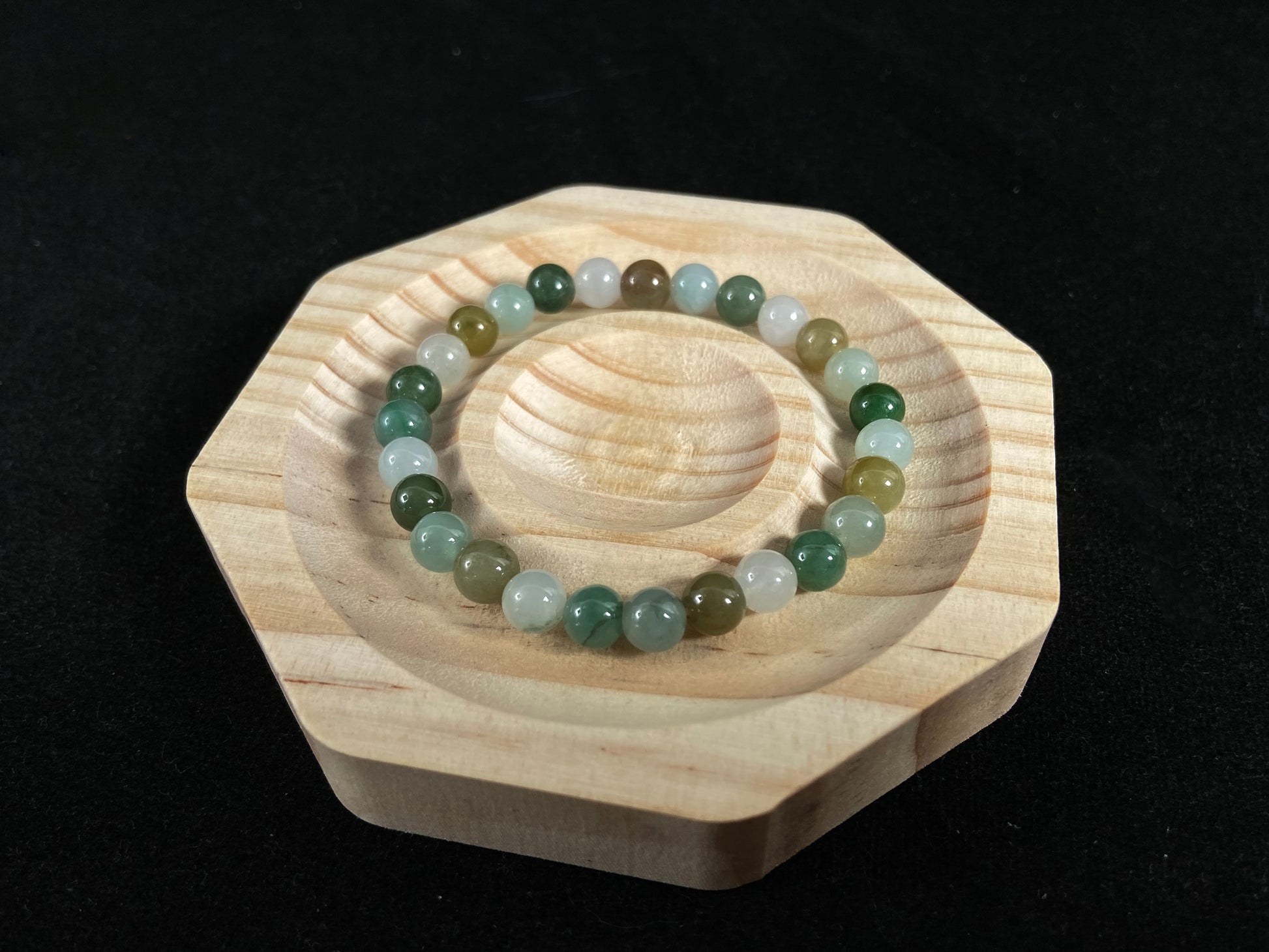 A strand of uniform jade beads in icy white, light green, deep green, pale yellow, and brown.
