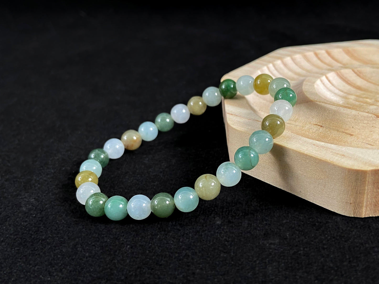 A strand of uniform jade beads in icy white, light green, deep green, pale yellow, and brown.