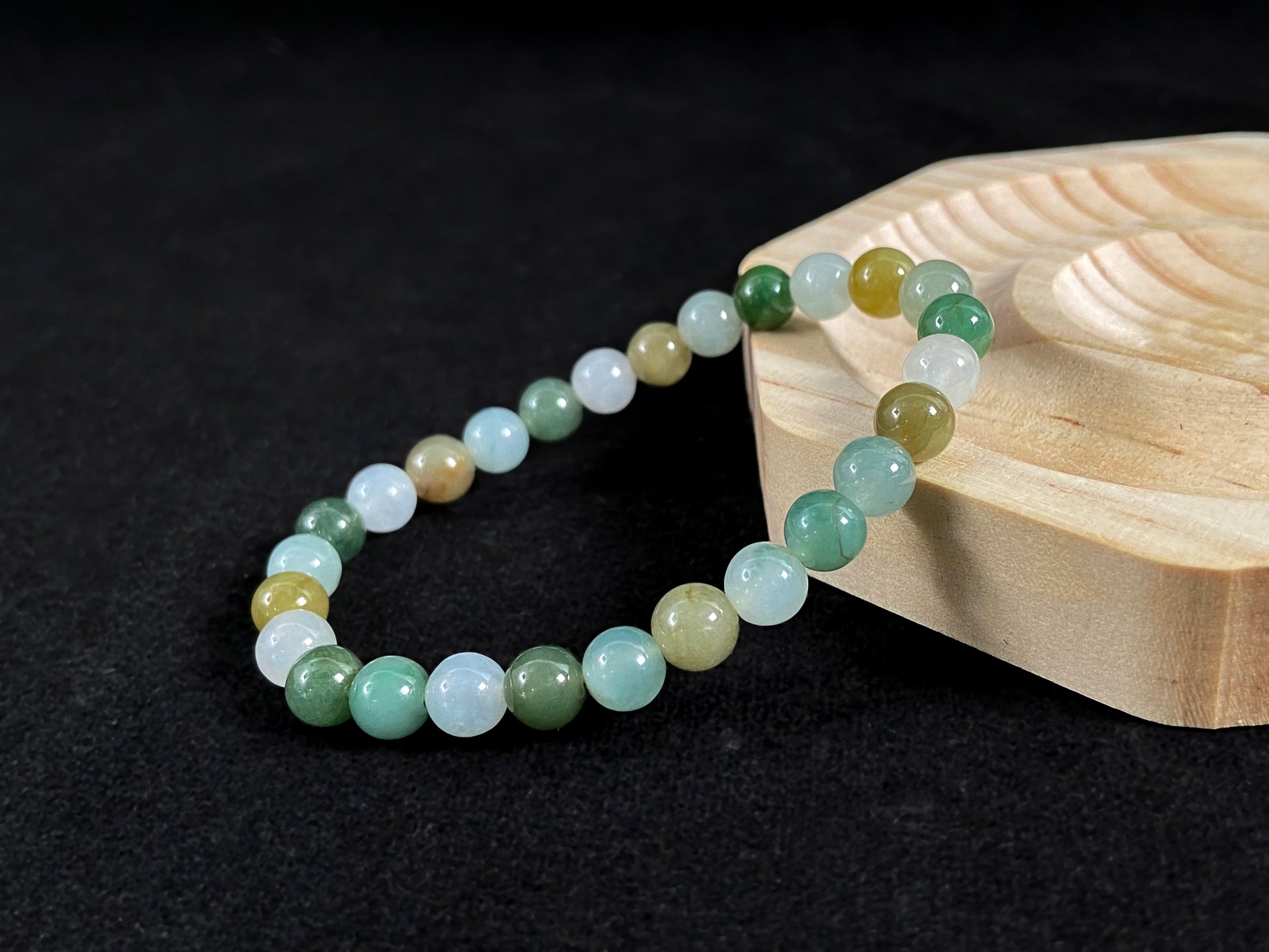 A strand of uniform jade beads in icy white, light green, deep green, pale yellow, and brown.