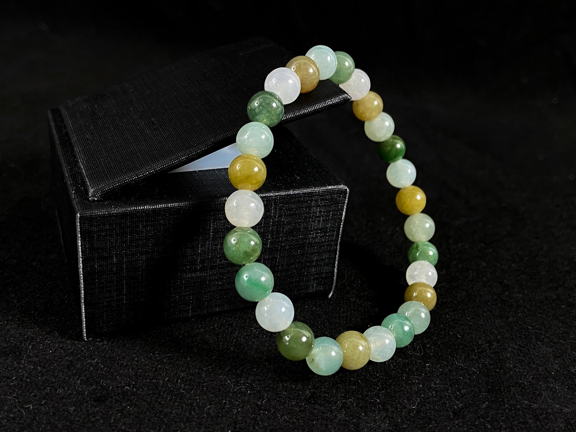 A strand of uniform jade beads in icy white, light green, deep green, pale yellow, and brown.