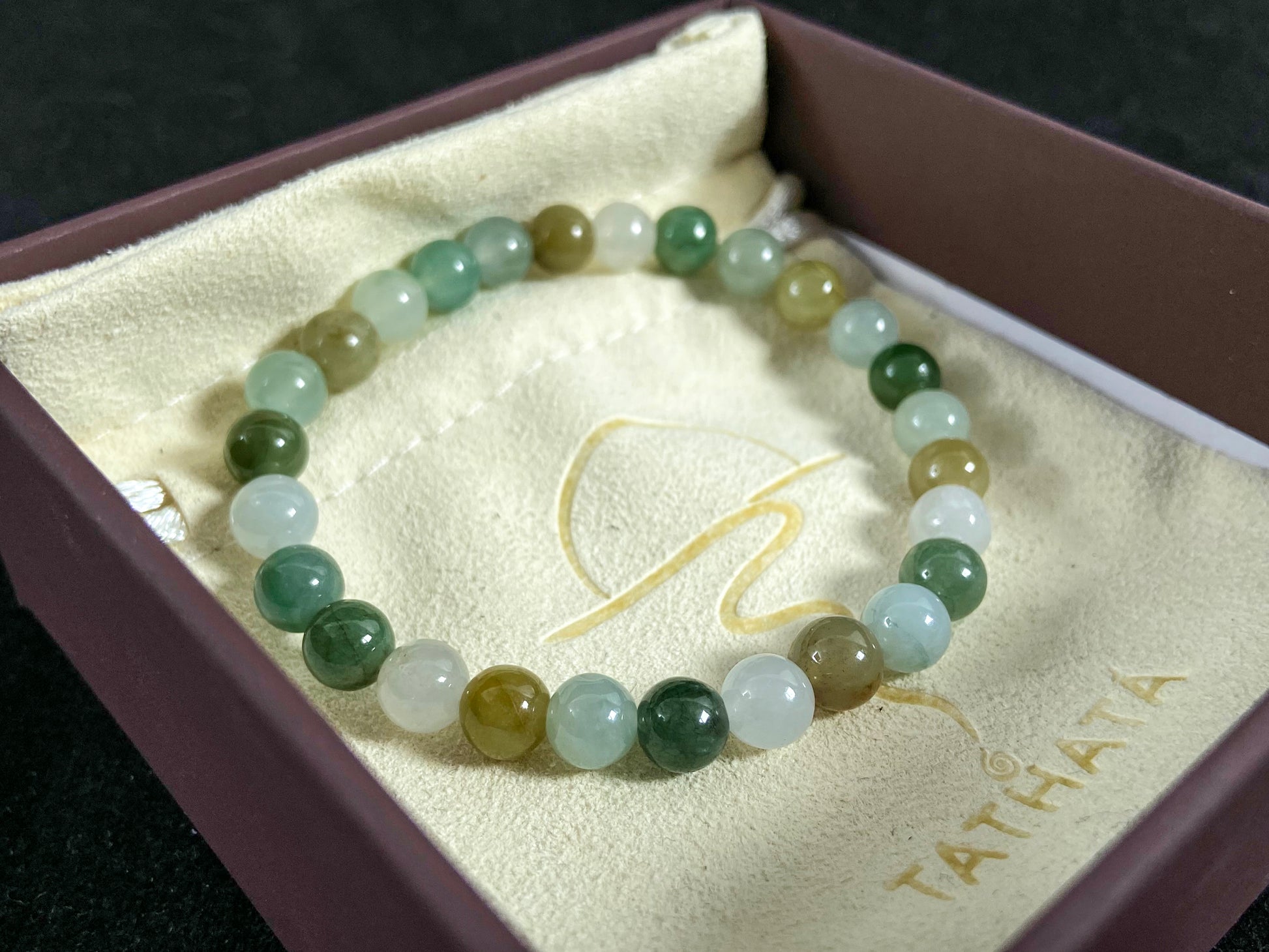 A strand of uniform jade beads in icy white, light green, deep green, pale yellow, and brown.