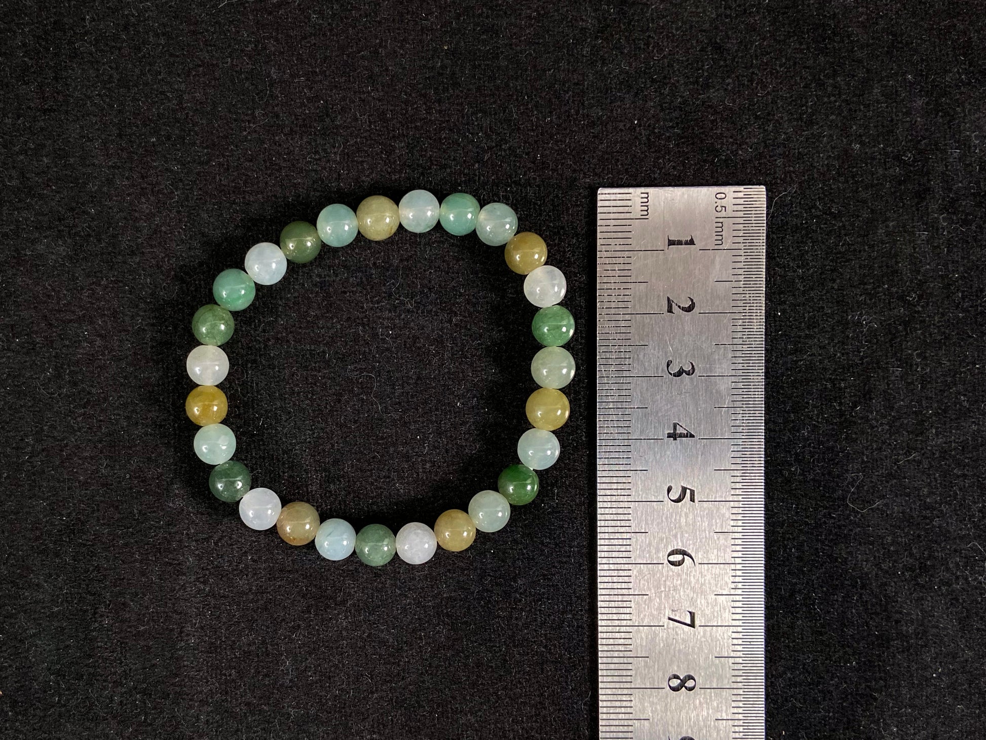 A strand of uniform jade beads in icy white, light green, deep green, pale yellow, and brown.