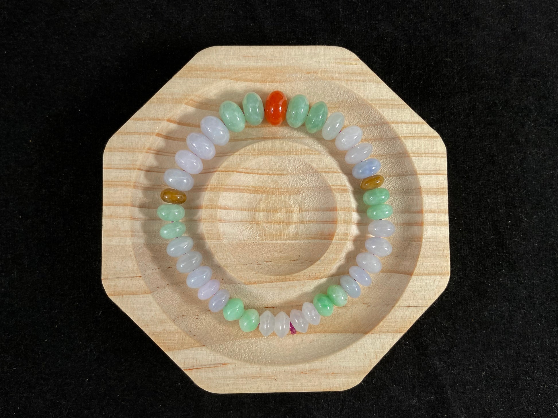 A jade bead strand with graduated sizing from the center, featuring white, green, brown, and red hues.