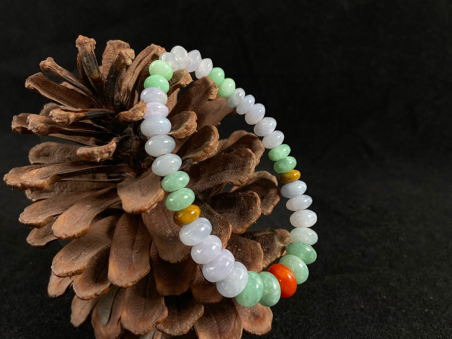 A jade bead strand with graduated sizing from the center, featuring white, green, brown, and red hues.