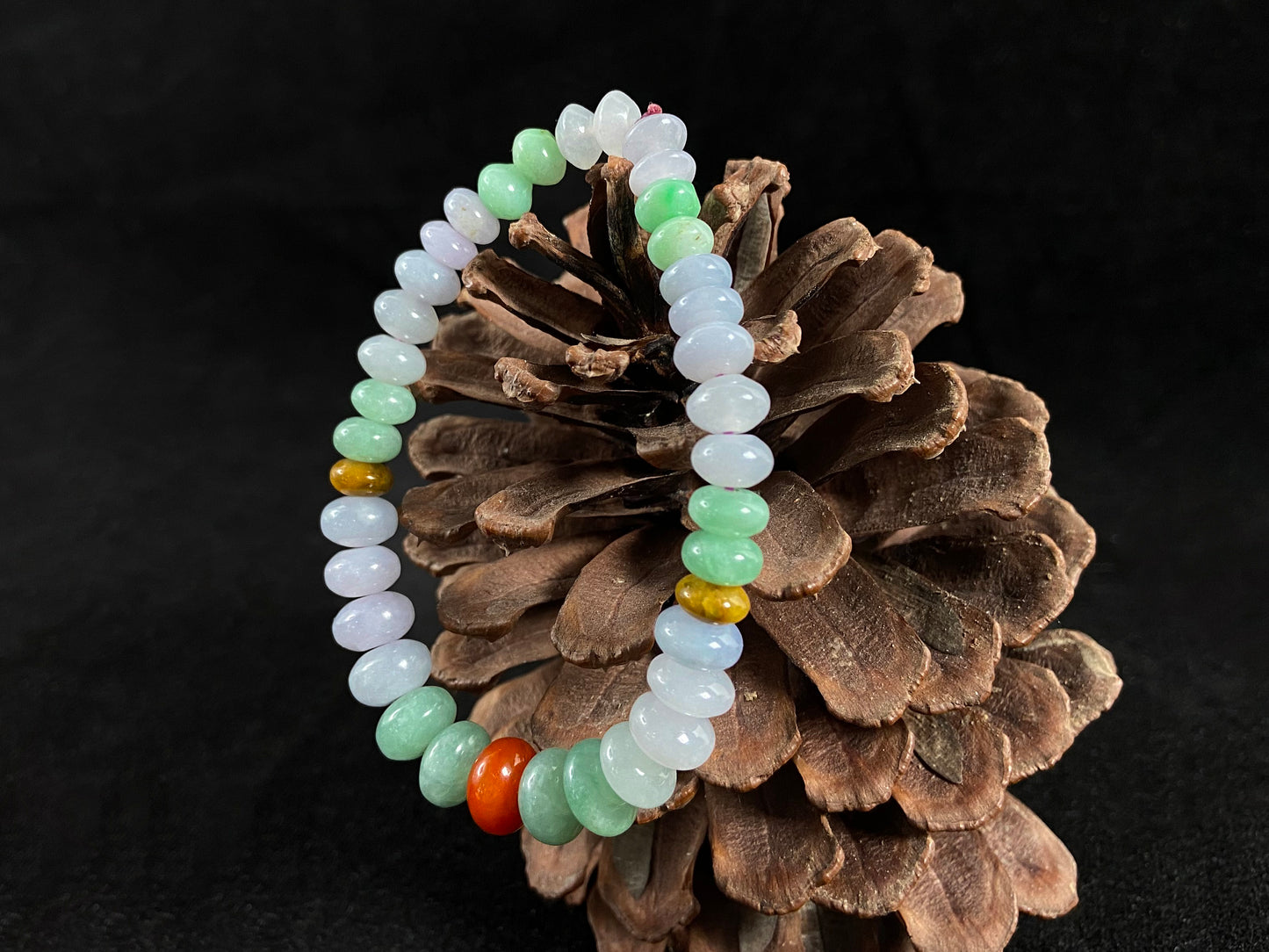 A jade bead strand with graduated sizing from the center, featuring white, green, brown, and red hues.