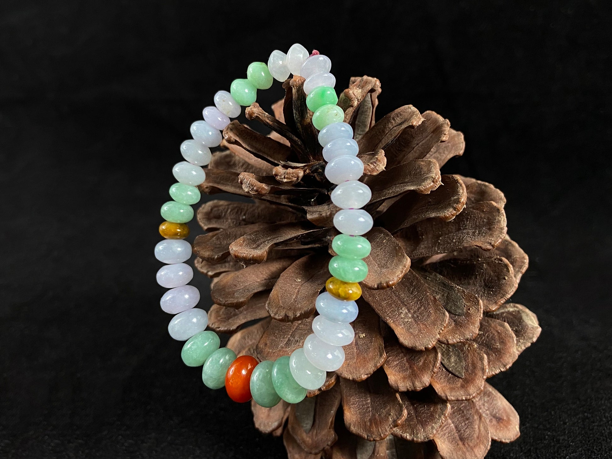 A jade bead strand with graduated sizing from the center, featuring white, green, brown, and red hues.