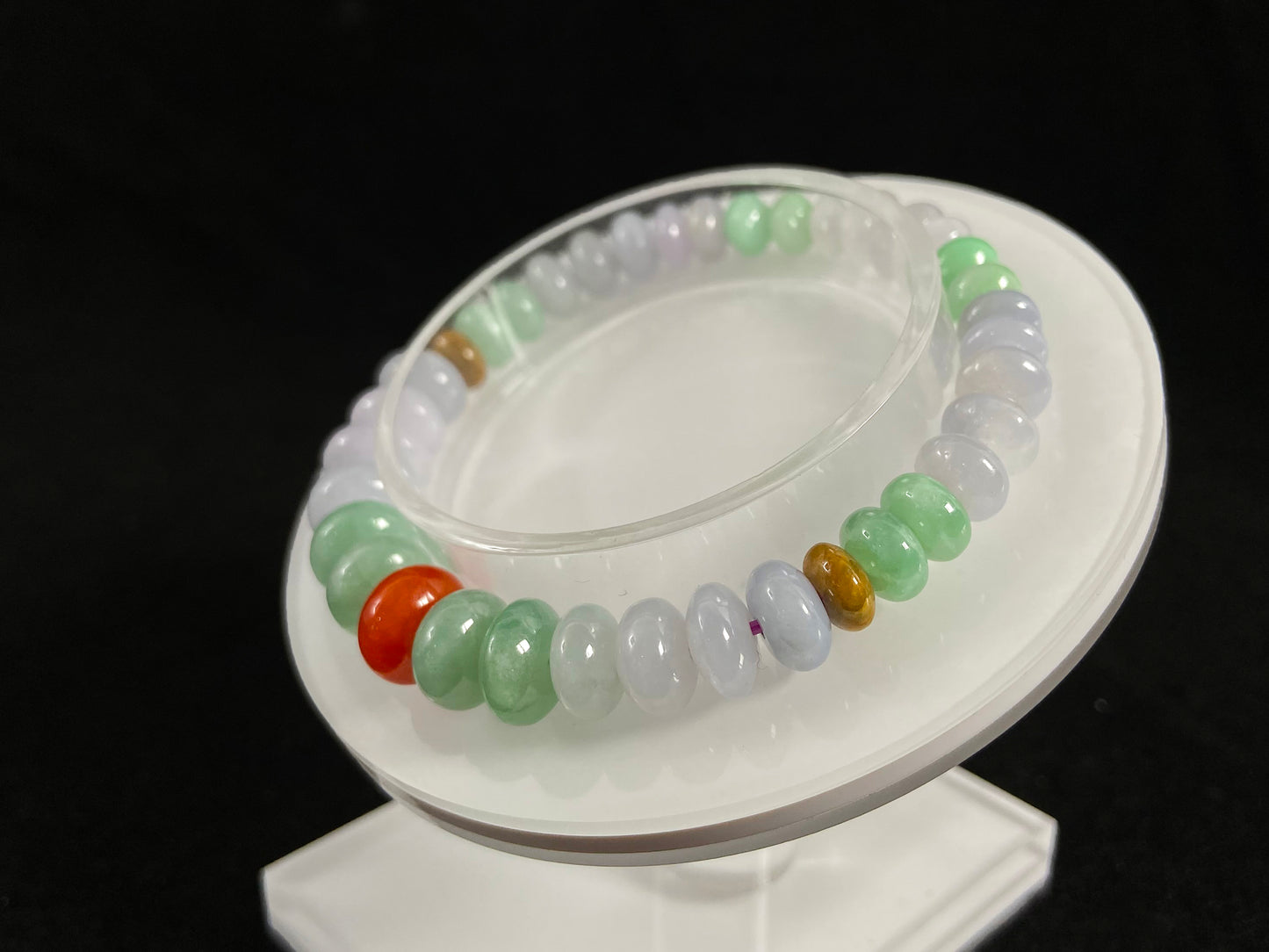 A jade bead strand with graduated sizing from the center, featuring white, green, brown, and red hues.