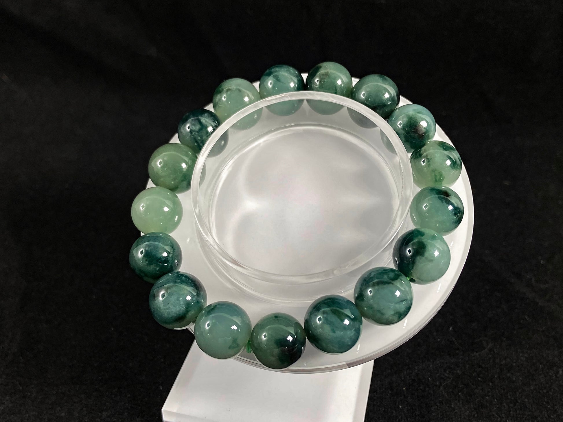 This jadeite bead strand has beads of the same size each translucent one with a soft white green base, dotted with dark green.