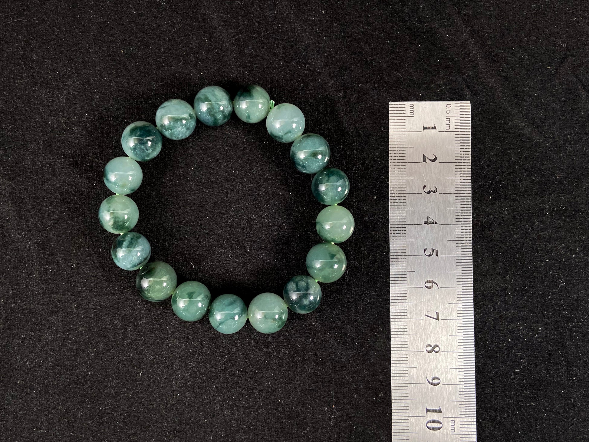 This jadeite bead strand has beads of the same size each translucent one with a soft white green base, dotted with dark green.
