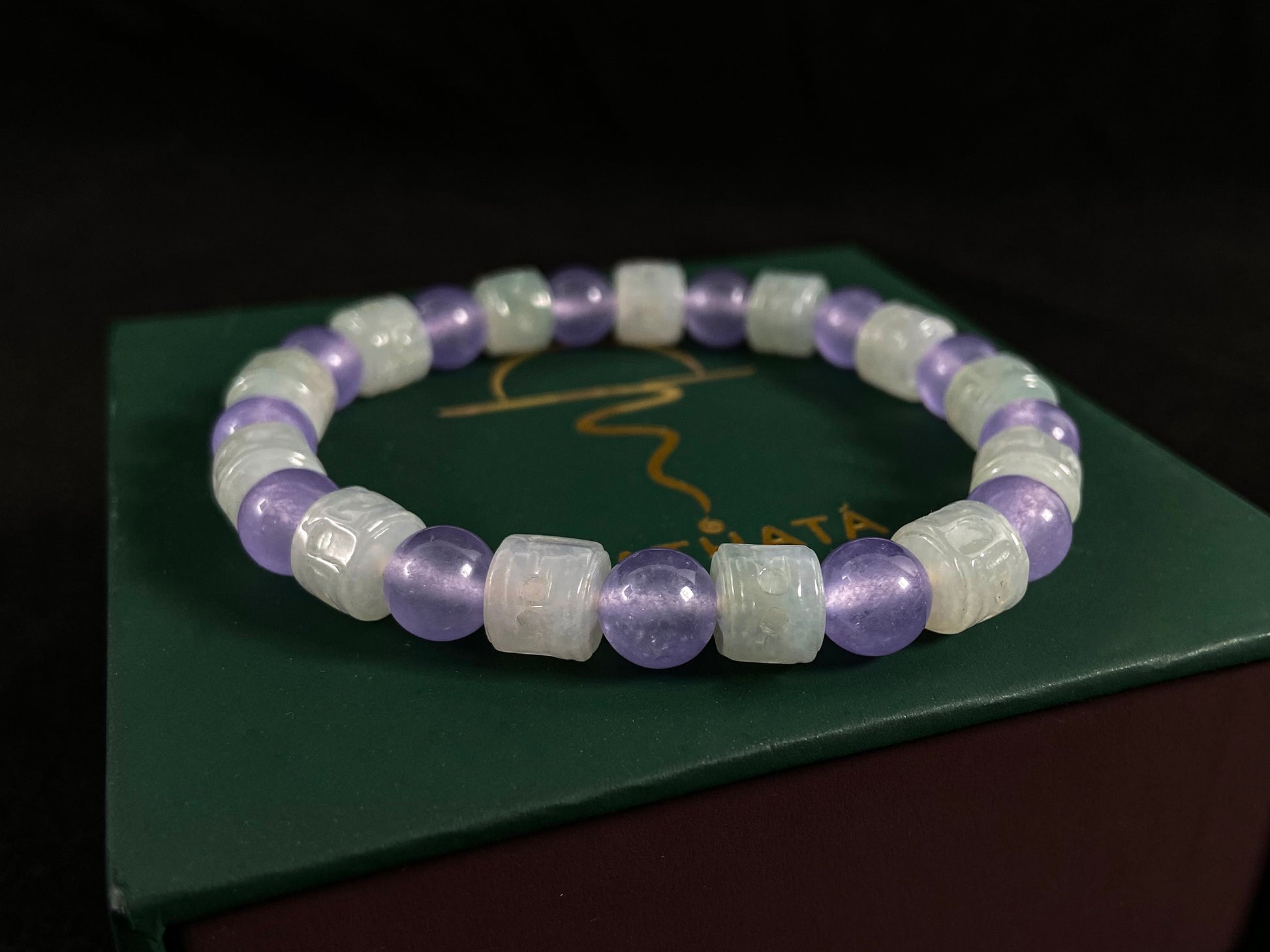 A jade bead strand featuring transparent purple spheres and semi transparent white cylinders.