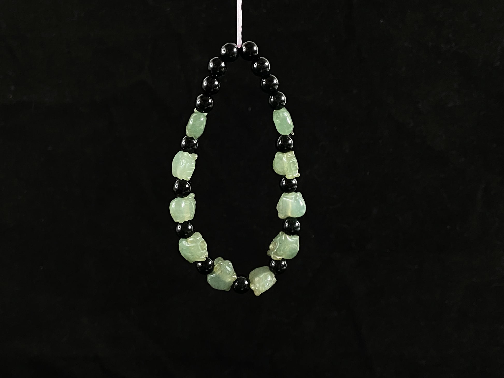 A jade bead strand featuring 17 black beads and 10 light green pig shaped beads.
