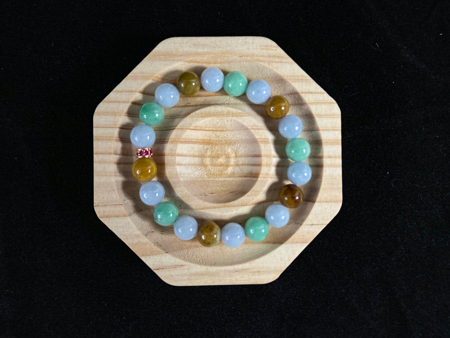 A jade bead strand combining yellow, brown, creamy white, and light green beads, accented with a rose gold alloy cylinder.