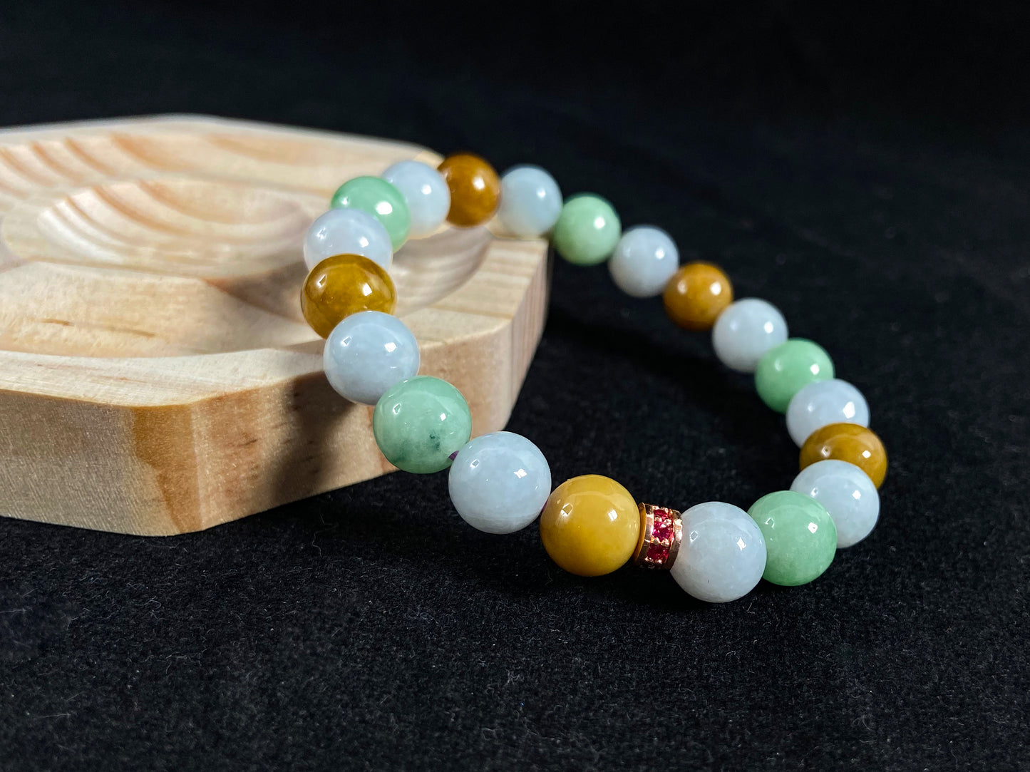 A jade bead strand combining yellow, brown, creamy white, and light green beads, accented with a rose gold alloy cylinder.