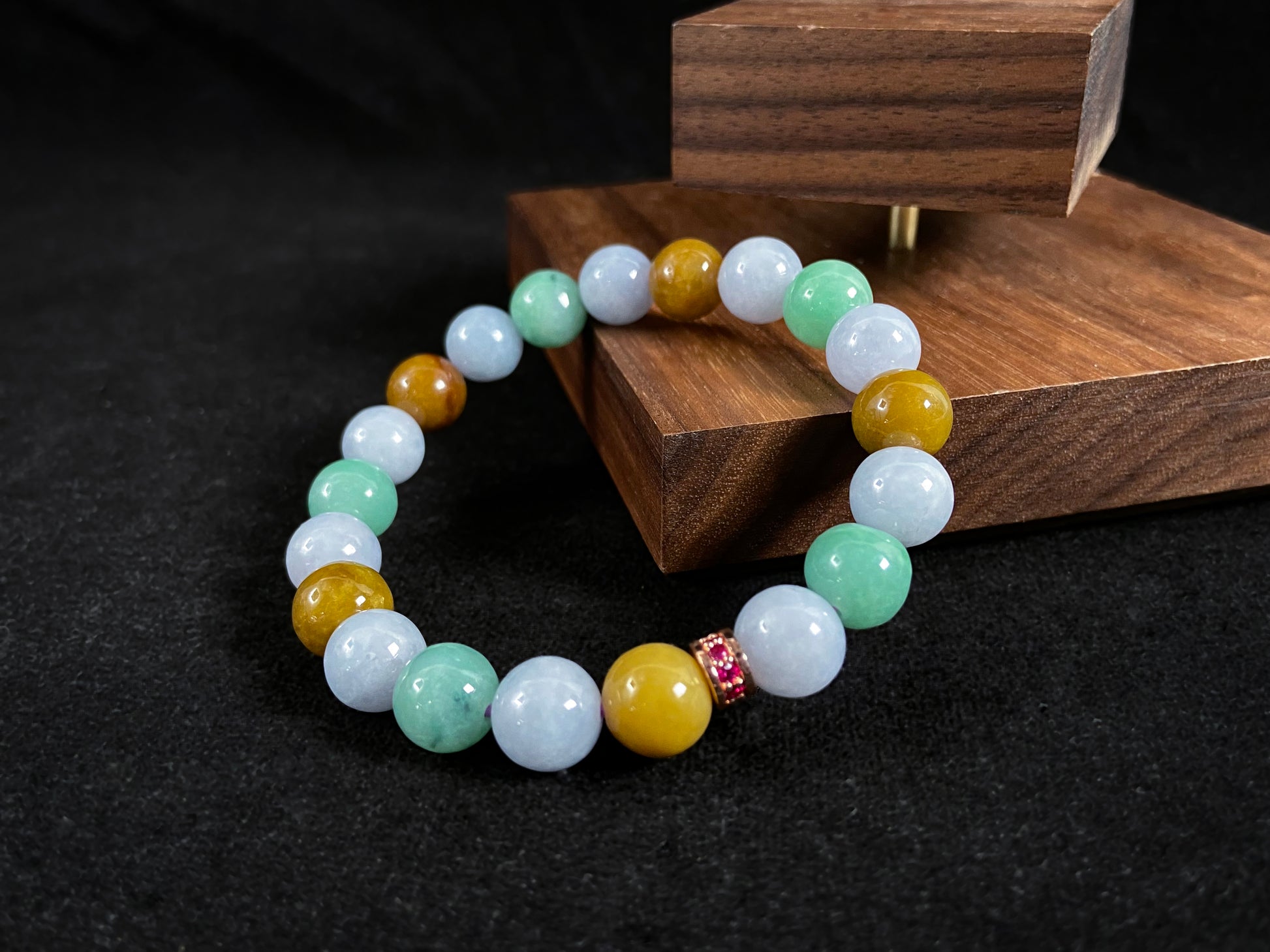 A jade bead strand combining yellow, brown, creamy white, and light green beads, accented with a rose gold alloy cylinder.