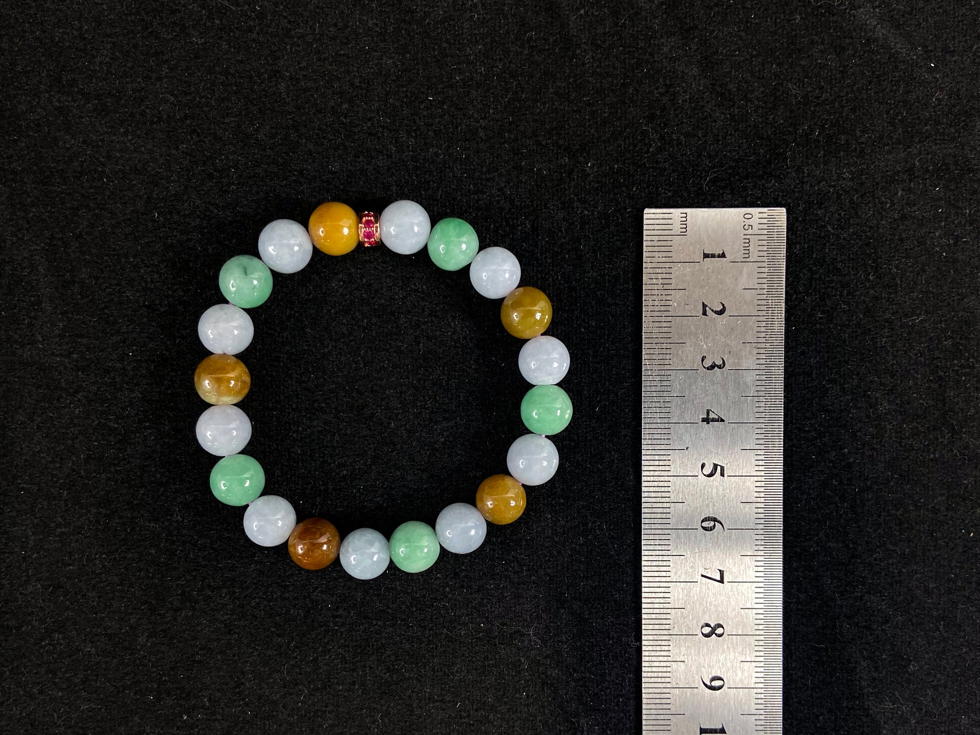 A jade bead strand combining yellow, brown, creamy white, and light green beads, accented with a rose gold alloy cylinder.