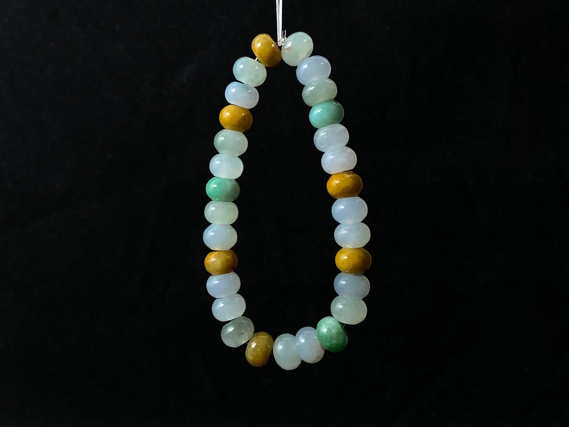 A jade bead strand featuring green, brown, yellow, white, and icy toned beads.