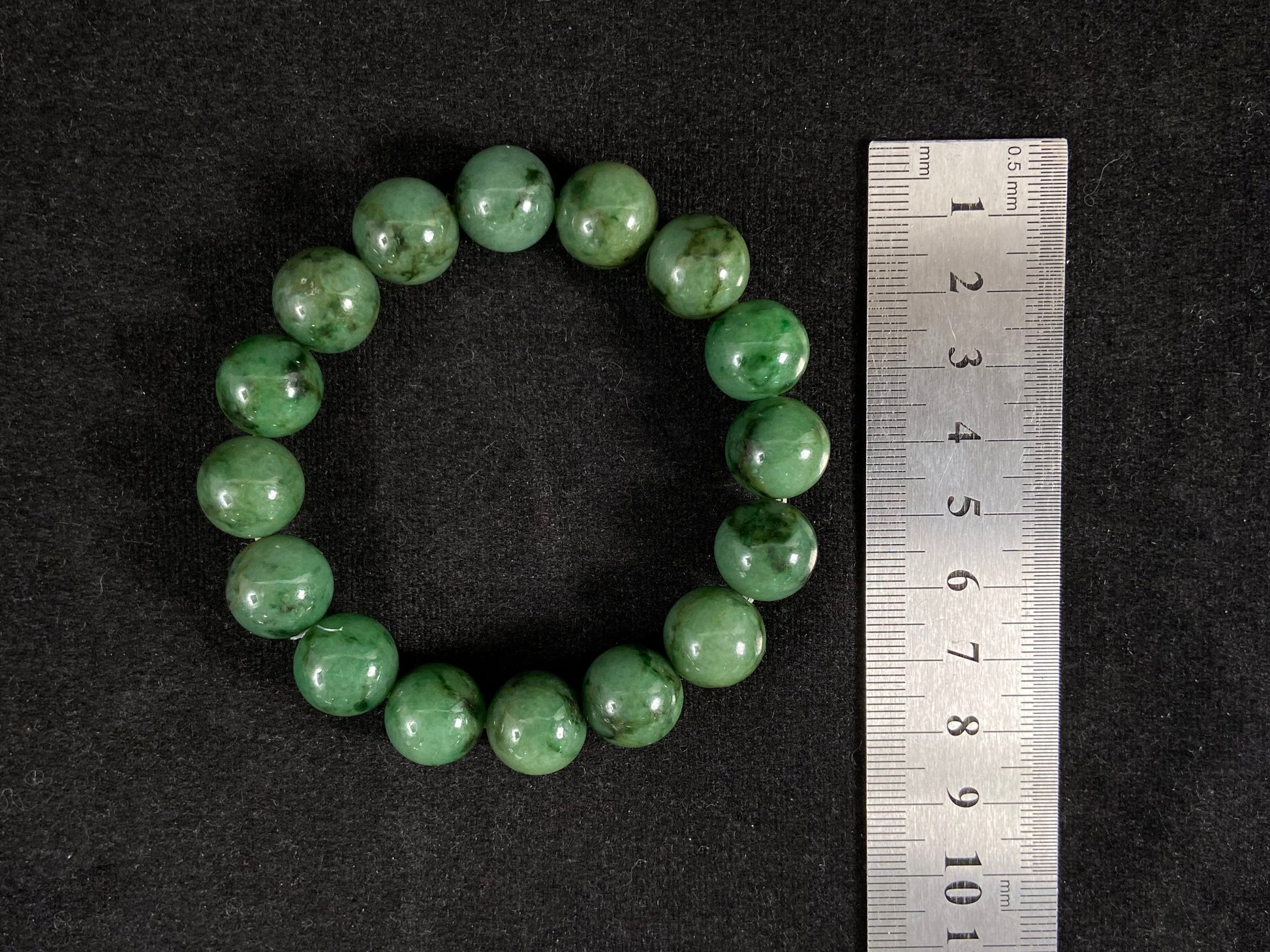 A strand of uniform jade beads in pale green with brownish green and deep green accents.