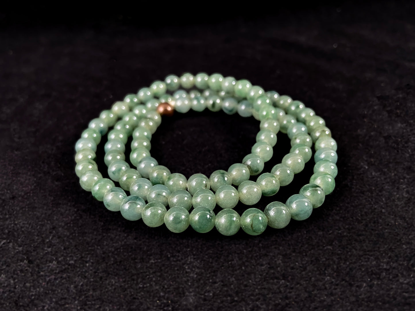 A strand of jade beads featuring a translucent light green base with deep green accents.