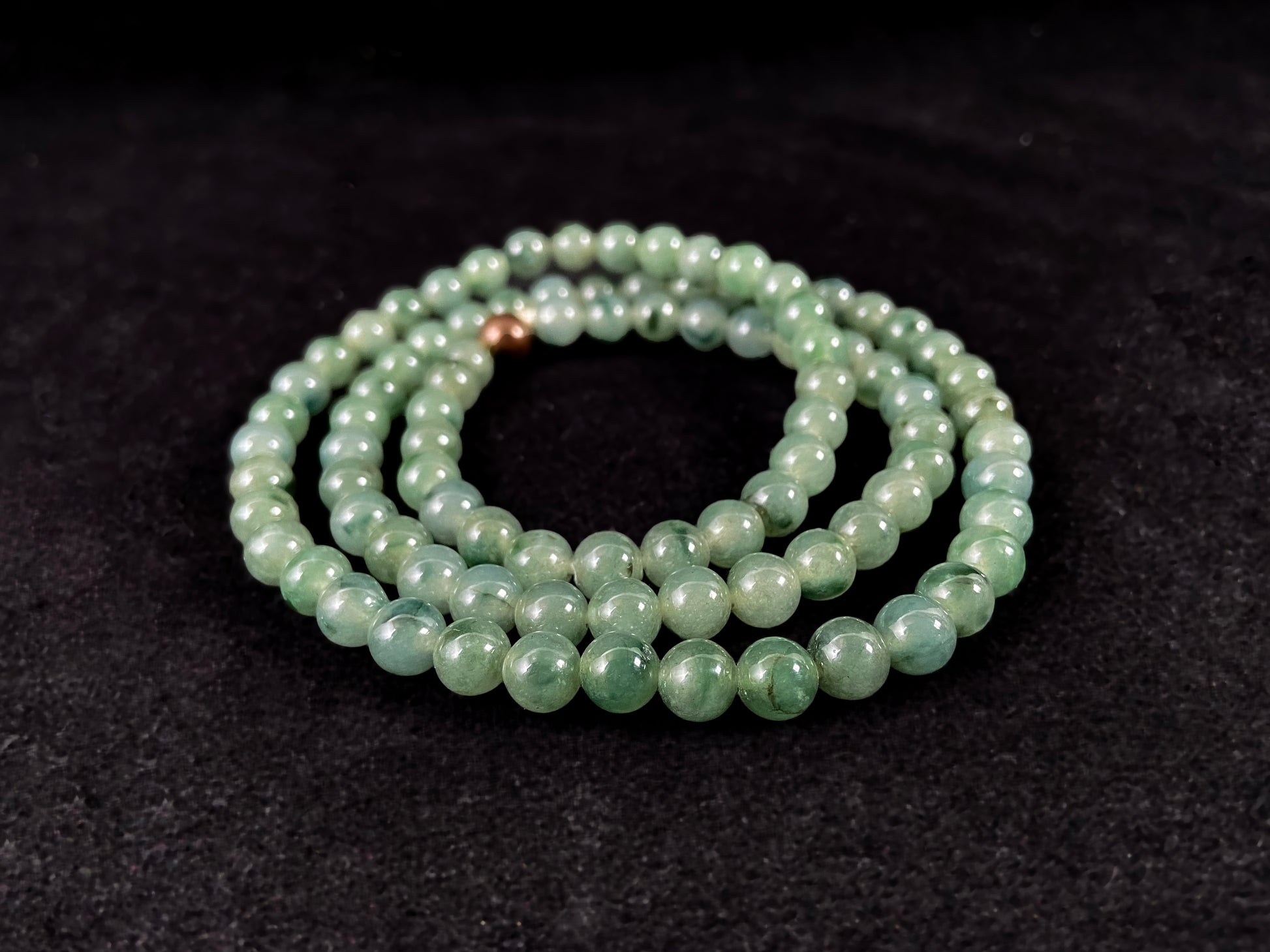 A strand of jade beads featuring a translucent light green base with deep green accents.