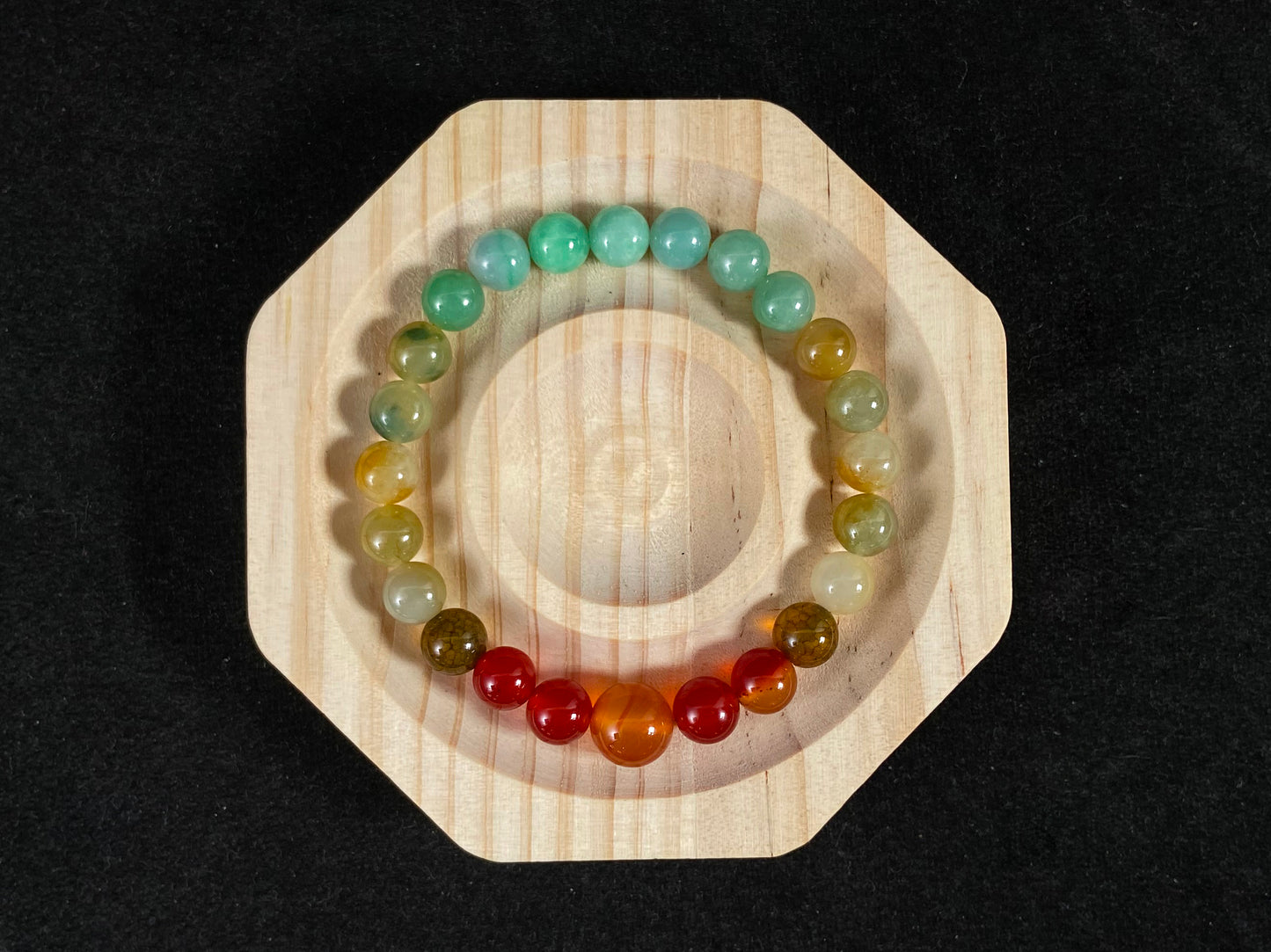 A jade bead strand with light green, brown, and red accent beads centered by a transparent orange focal bead.