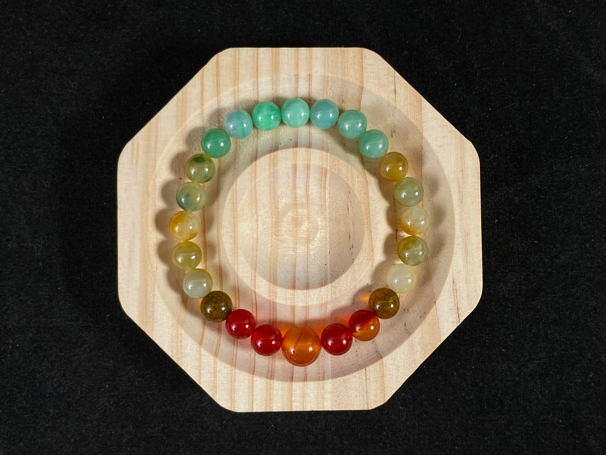 A jade bead strand with light green, brown, and red accent beads centered by a transparent orange focal bead.