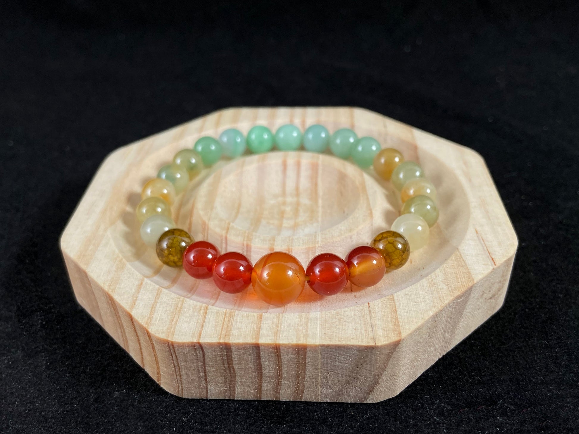 A jade bead strand with light green, brown, and red accent beads centered by a transparent orange focal bead.