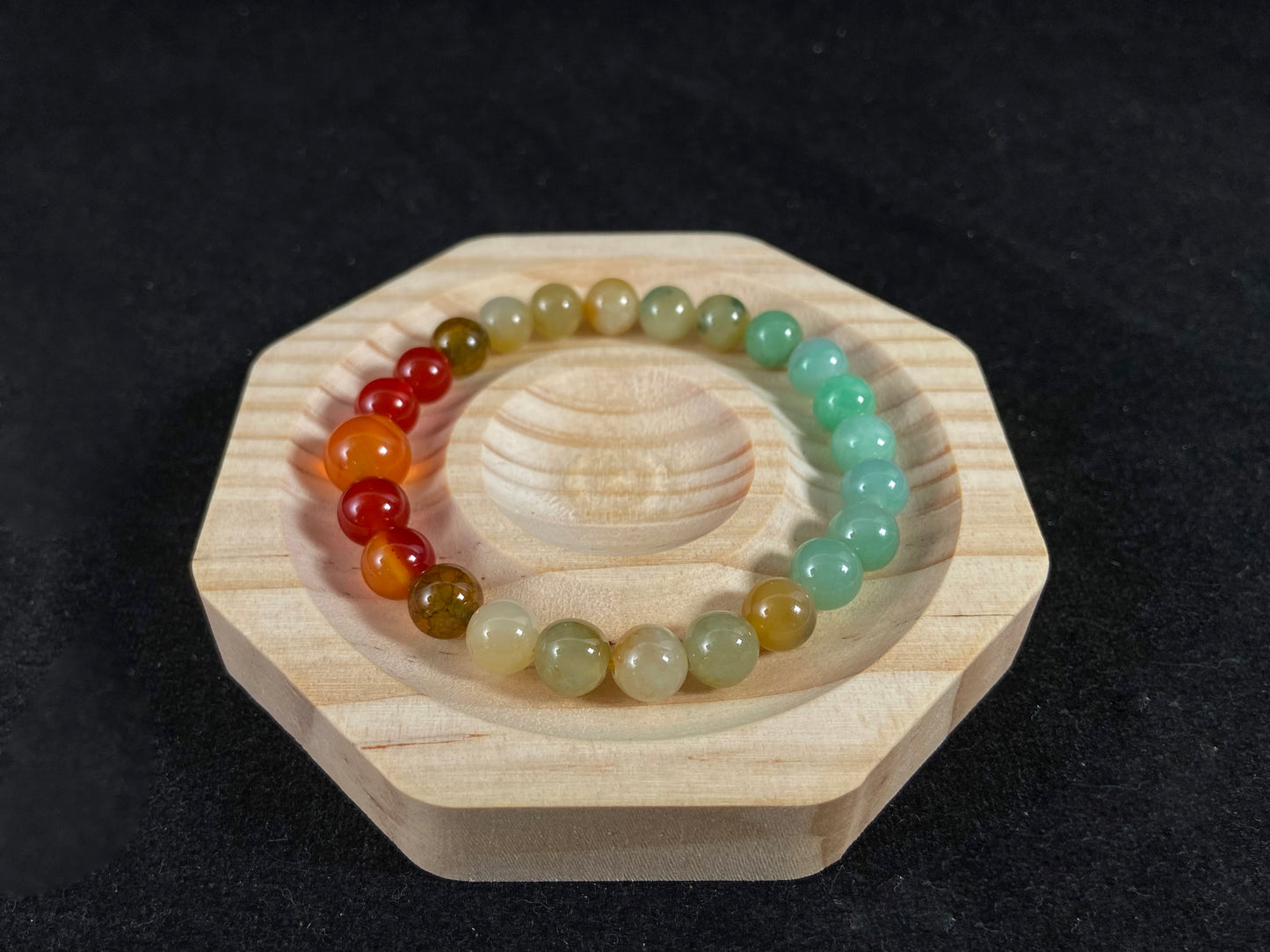 A jade bead strand with light green, brown, and red accent beads centered by a transparent orange focal bead.