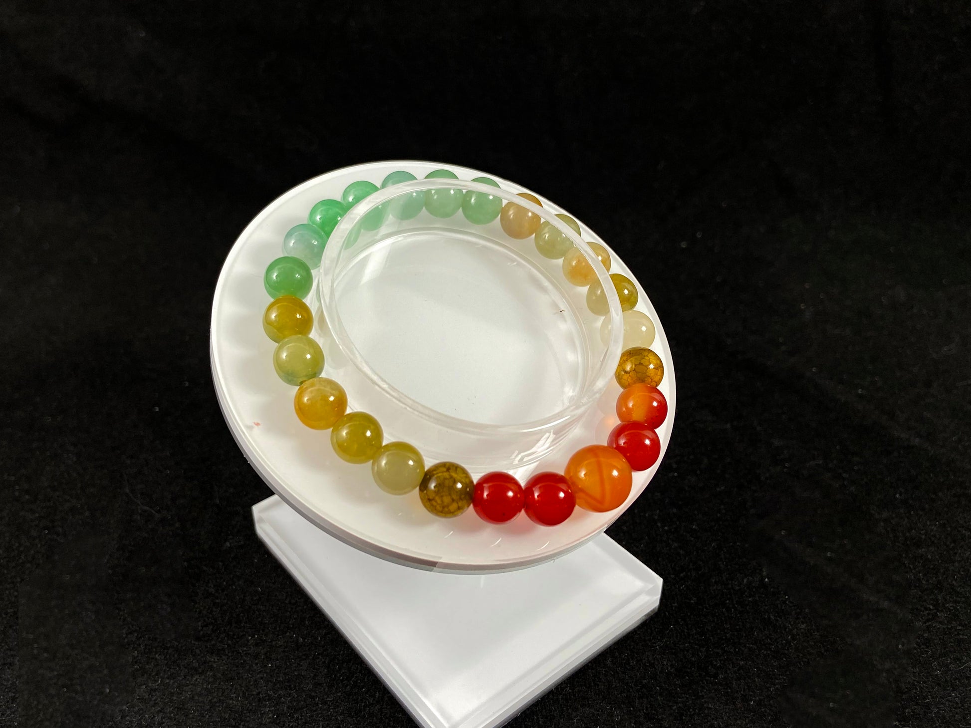 A jade bead strand with light green, brown, and red accent beads centered by a transparent orange focal bead.