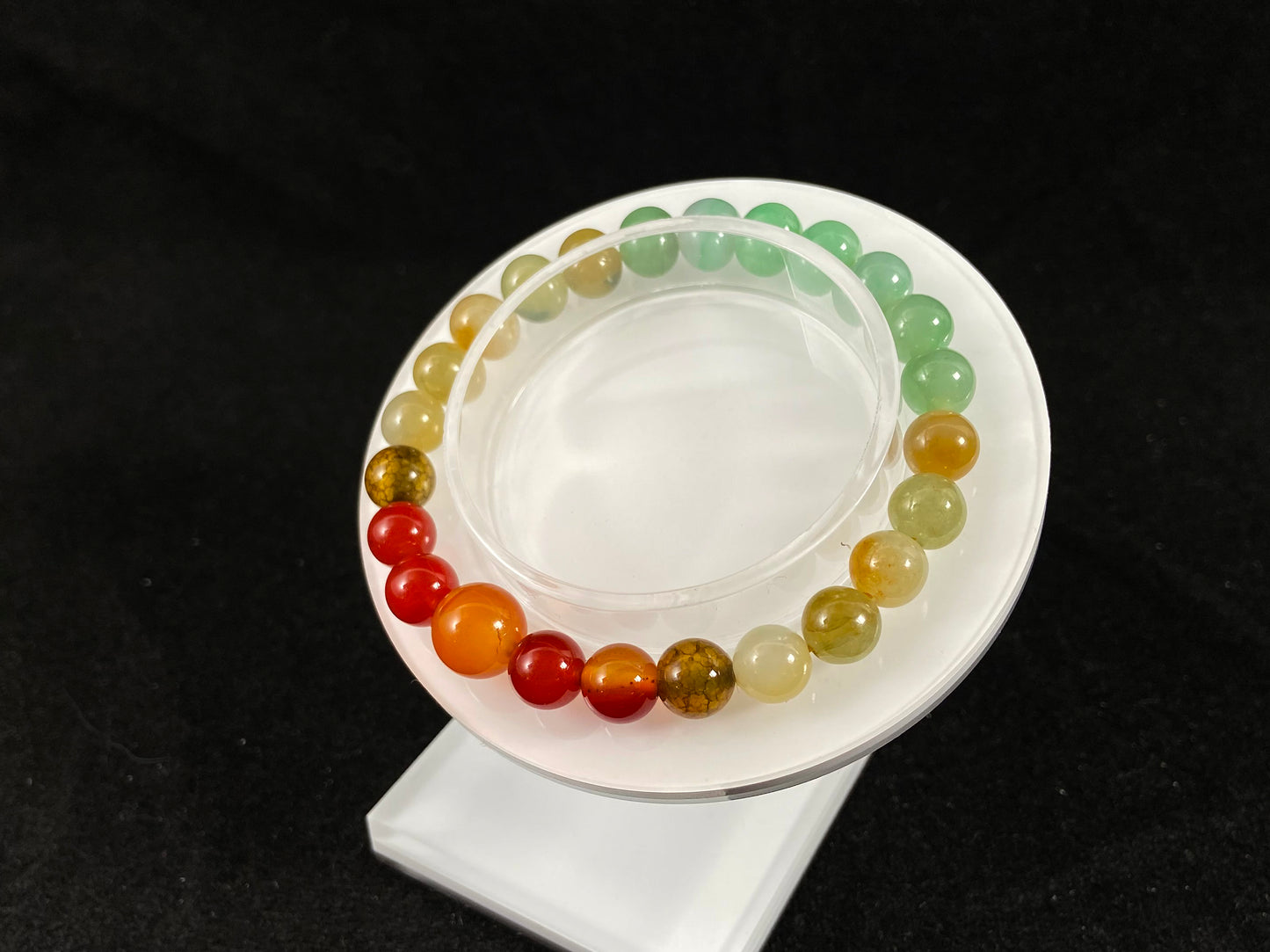 A jade bead strand with light green, brown, and red accent beads centered by a transparent orange focal bead.