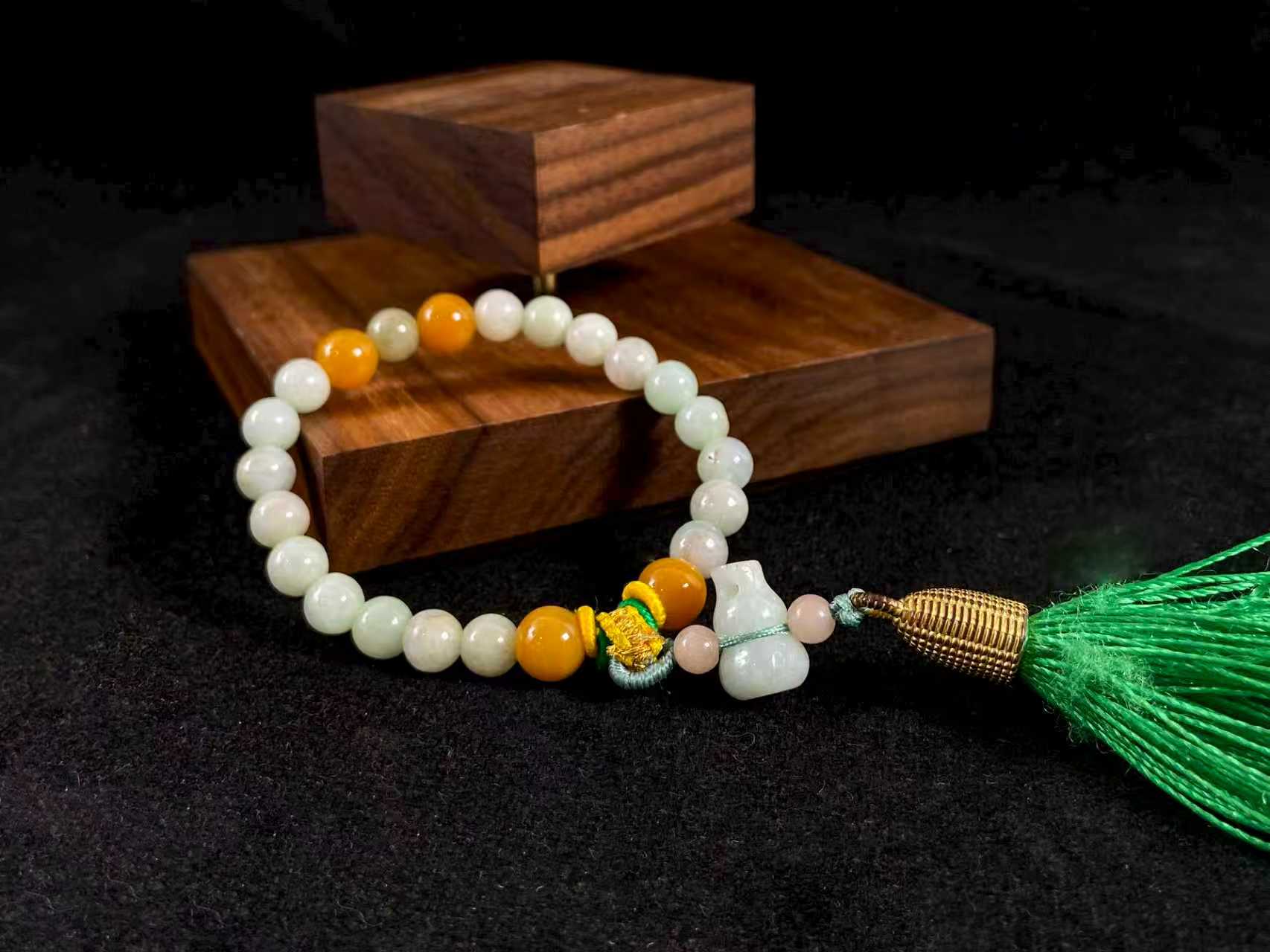 A milky white jade strand with gold, brown, and pink beads, gourd pendant, and green tassel.