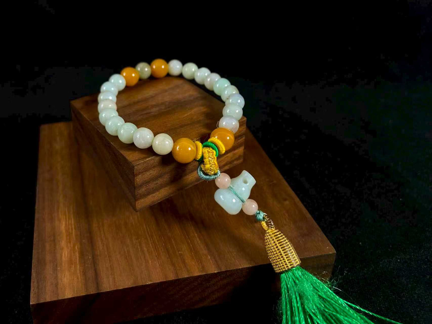 A milky white jade strand with gold, brown, and pink beads, gourd pendant, and green tassel.